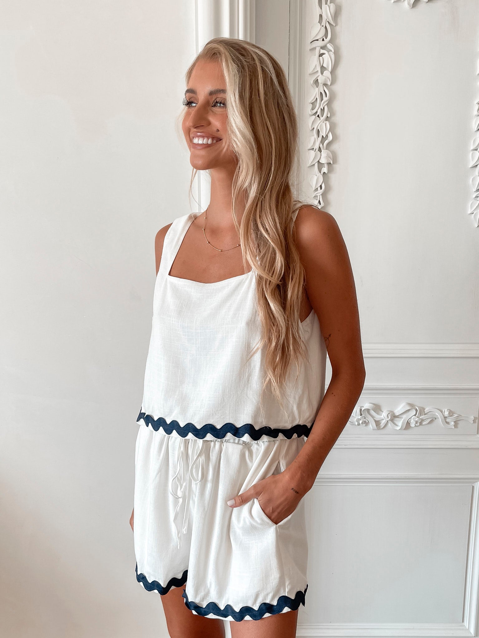 A woman wearing a white crop top with a square neckline and semi-relaxed fit, in a room with classic decor.