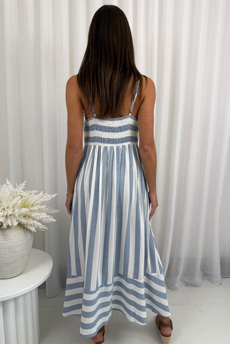 Woman wearing a blue and white striped dress standing in front of white curtains.