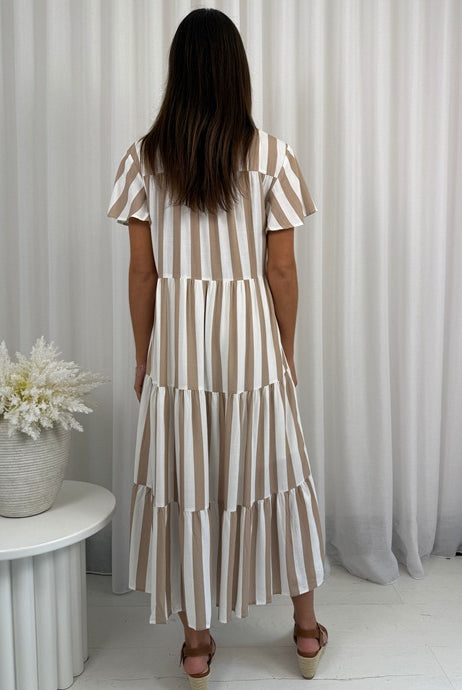 Woman wearing a striped dress standing in a room with white curtains and a small table with a plant.