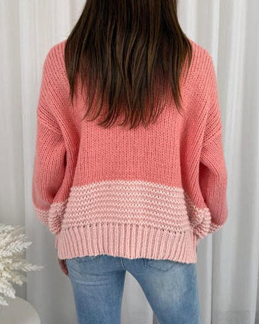 Person wearing a pink knitted sweater and jeans against a white curtain background