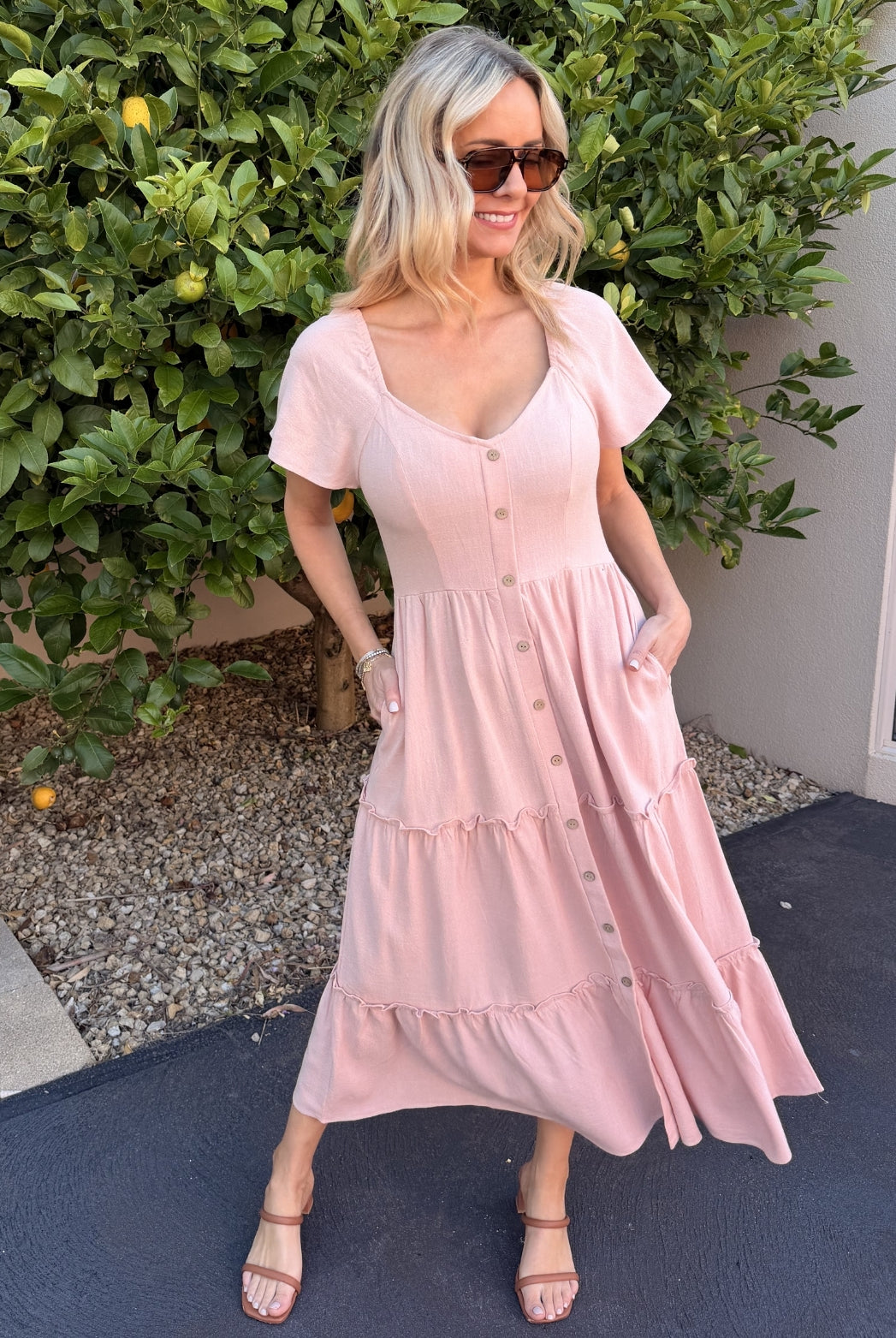 Women wearing the Celie Dress in Pink, a relaxed linen midi dress with V-neckline and tiered detail