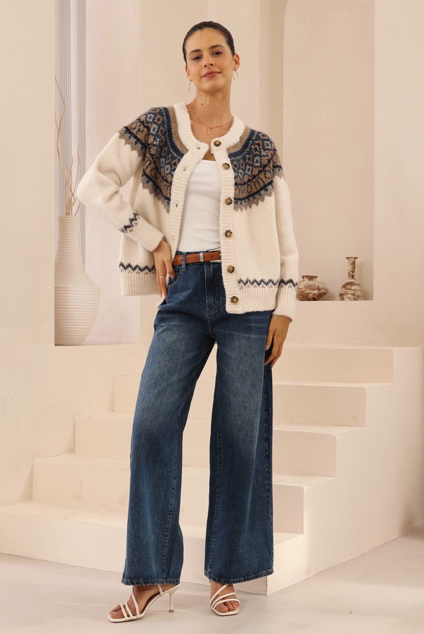 Woman wearing a patterned cardigan, white shirt, and blue jeans in an indoor setting.
