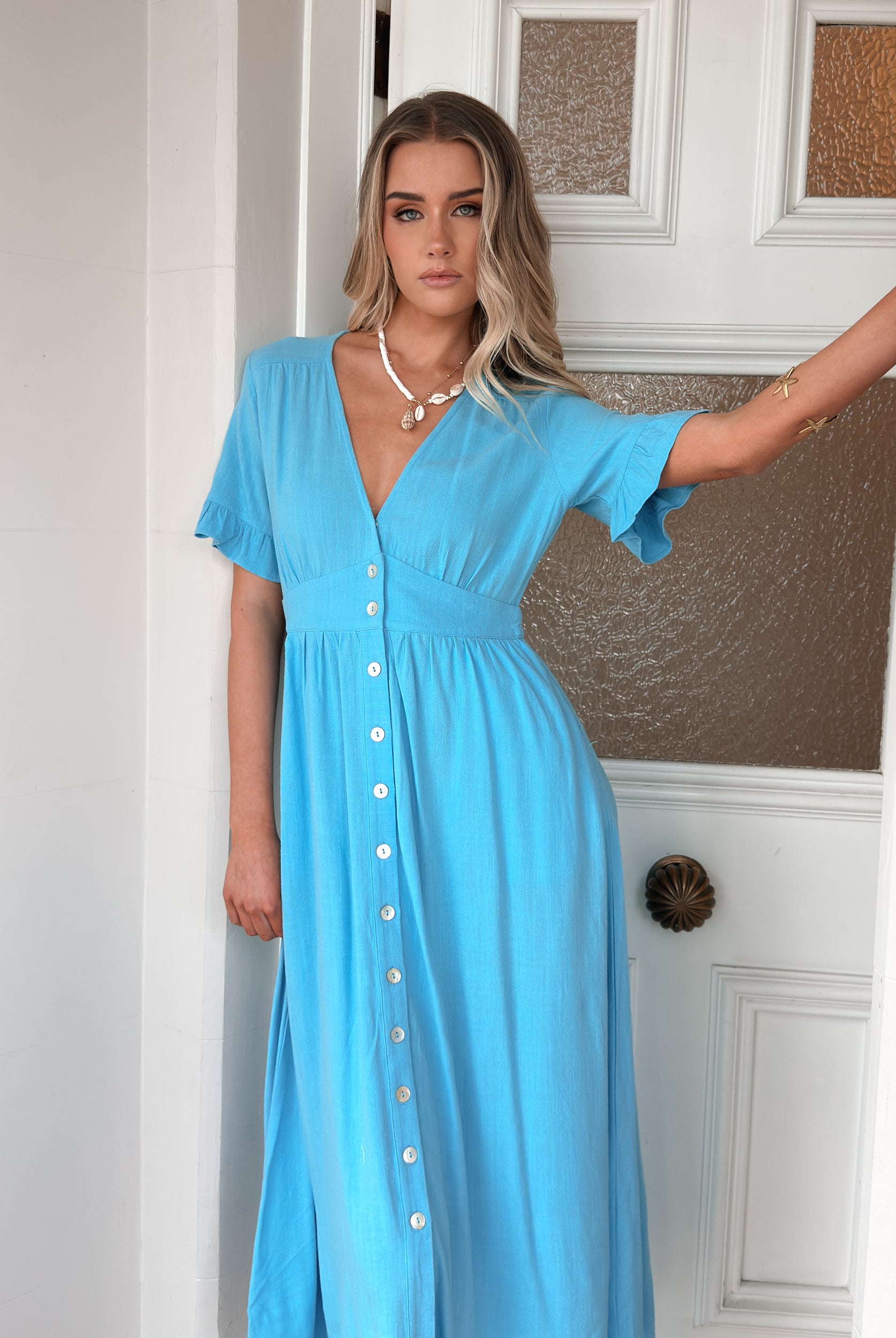 Women wearing the Korbela Dress in Sky Blue, a relaxed linen midi dress with V-neckline and button-up front