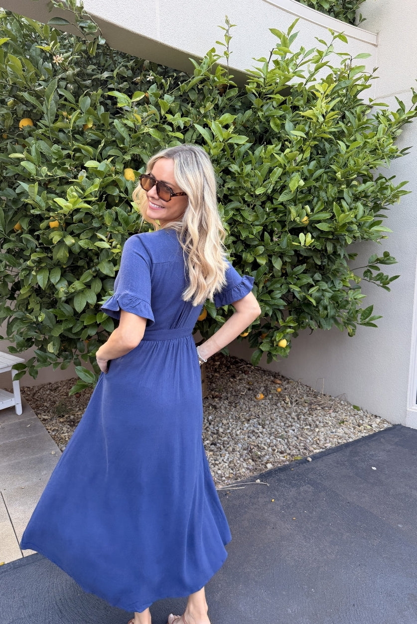 Side view of the Korbela Dress in Navy showing the flowing midi length and spot print fabric