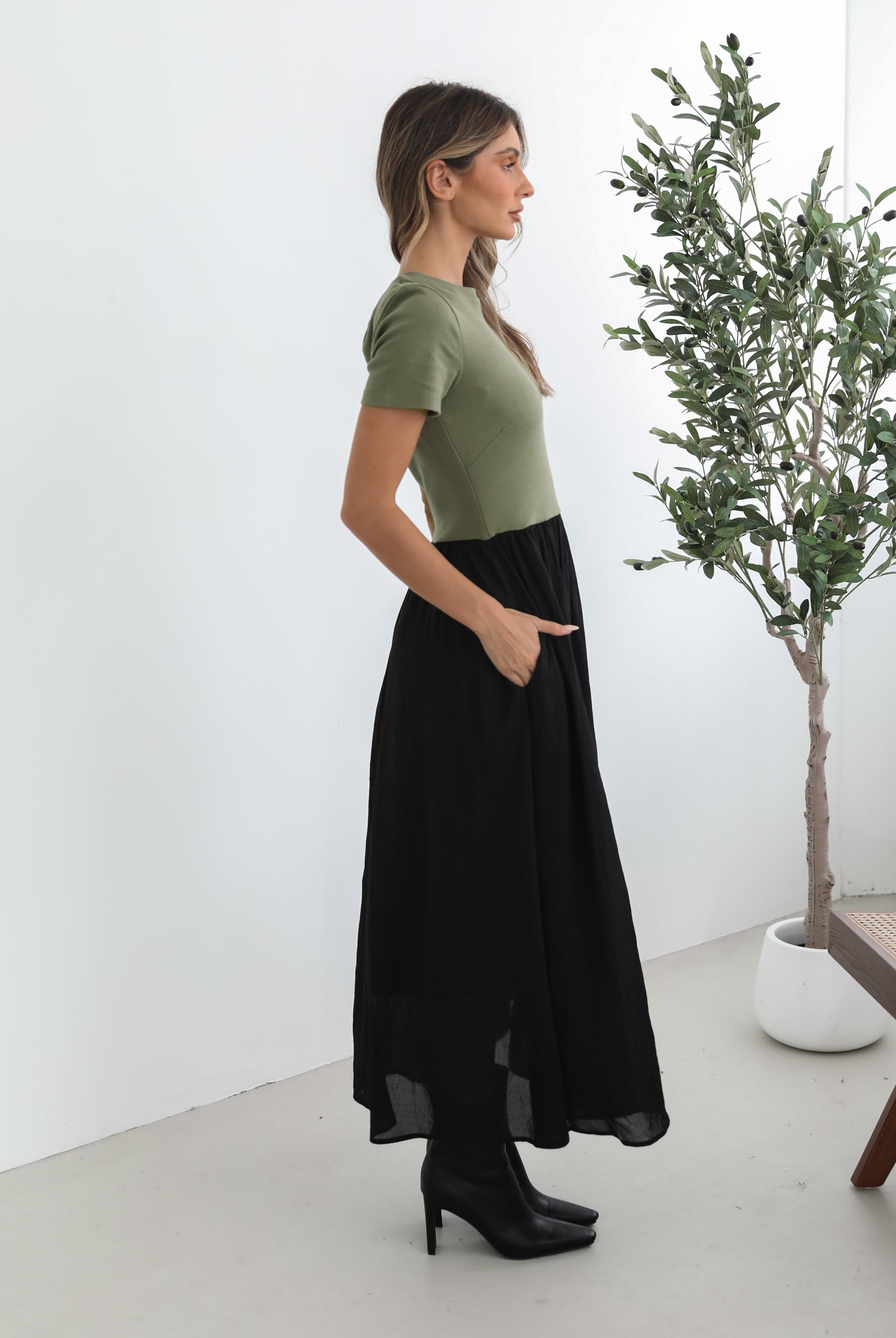 woman wearing a short sleeve round neck dress with green top and black flowy skirt paired with black boots in a white background studio