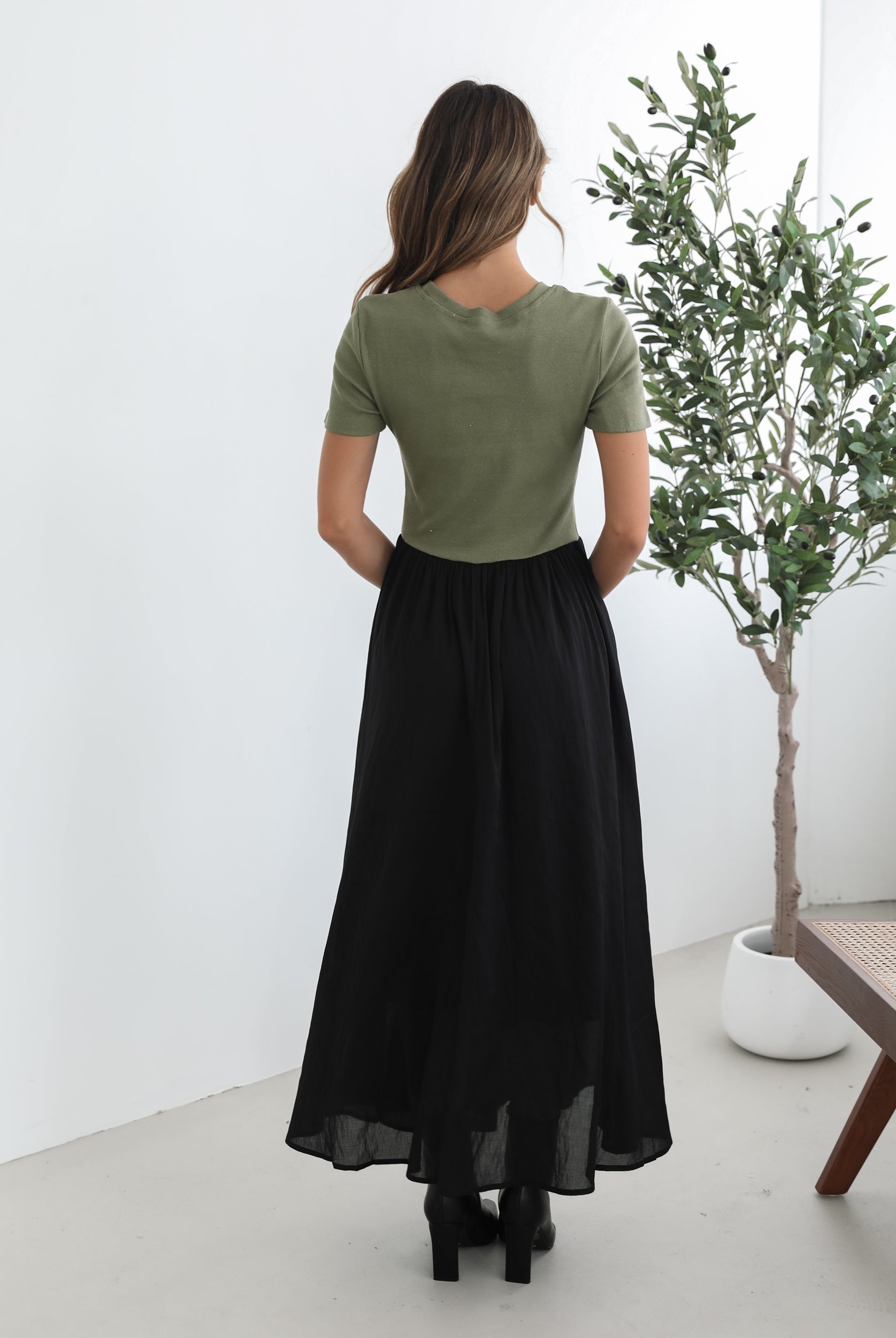 woman wearing a short sleeve round neck dress with green top and black flowy skirt paired with black boots in a white background studio