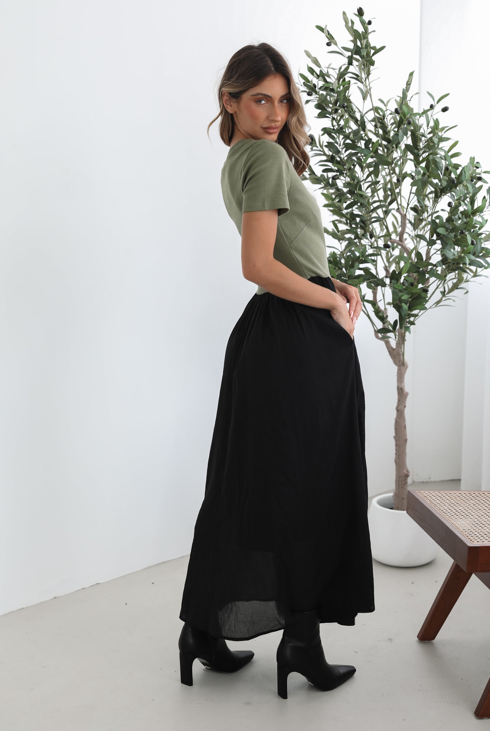 woman wearing a short sleeve round neck dress with green top and black flowy skirt paired with black boots in a white background studio