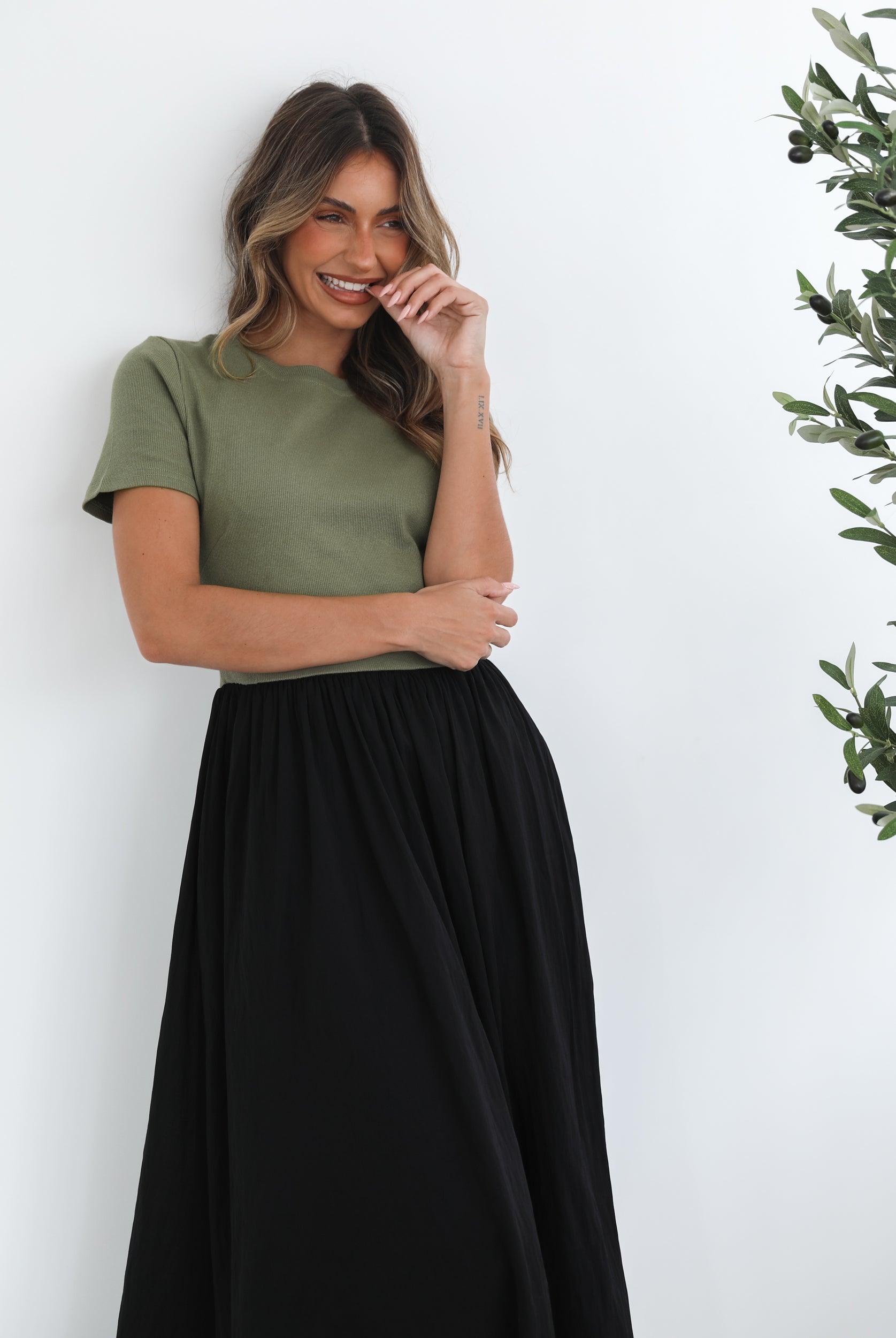 woman wearing a short sleeve round neck dress with green top and black flowy skirt paired with black boots in a white background studio