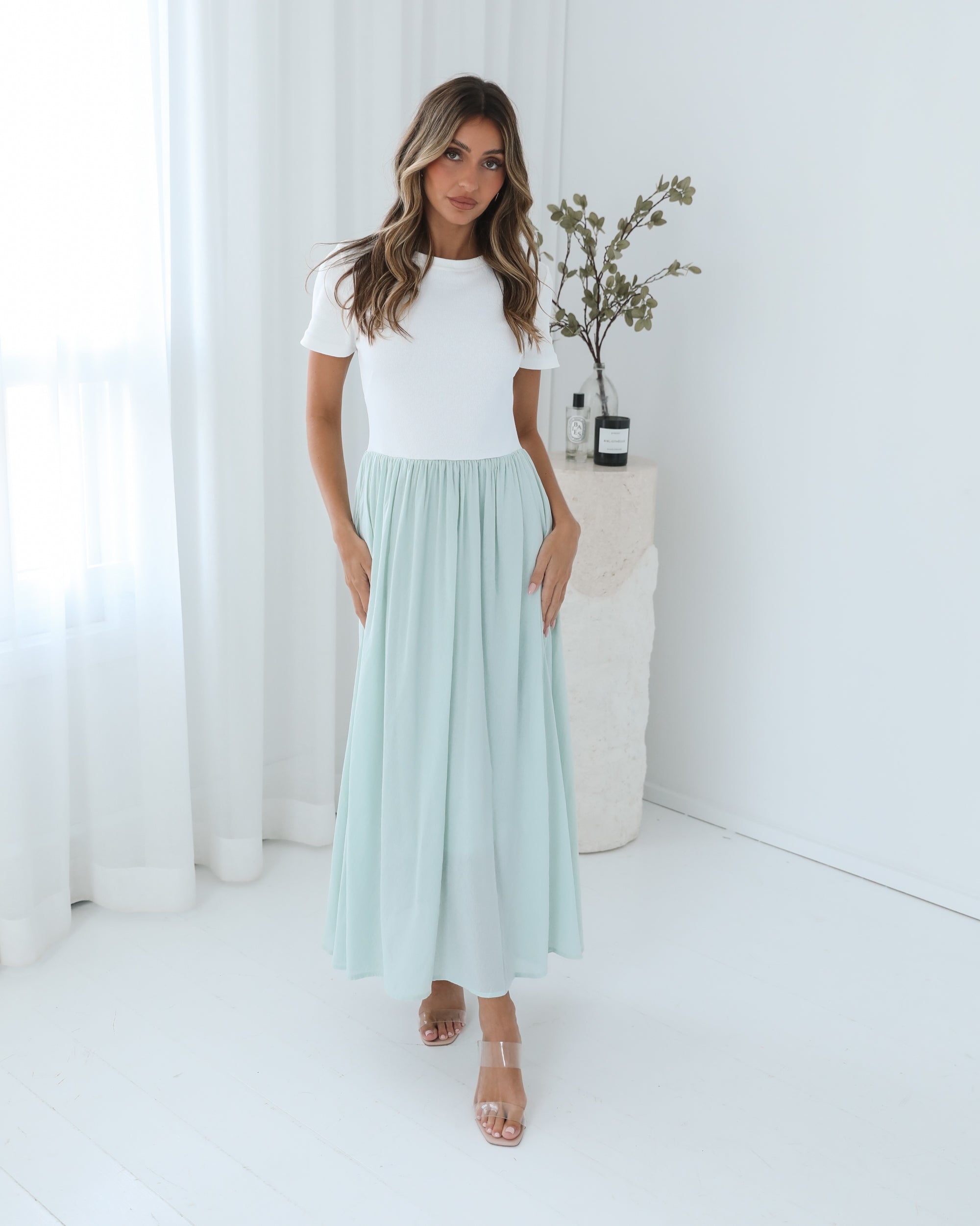 A woman wearing a knee-length dress with a round neckline and short sleeves. The dress is primarily white with sage green details.