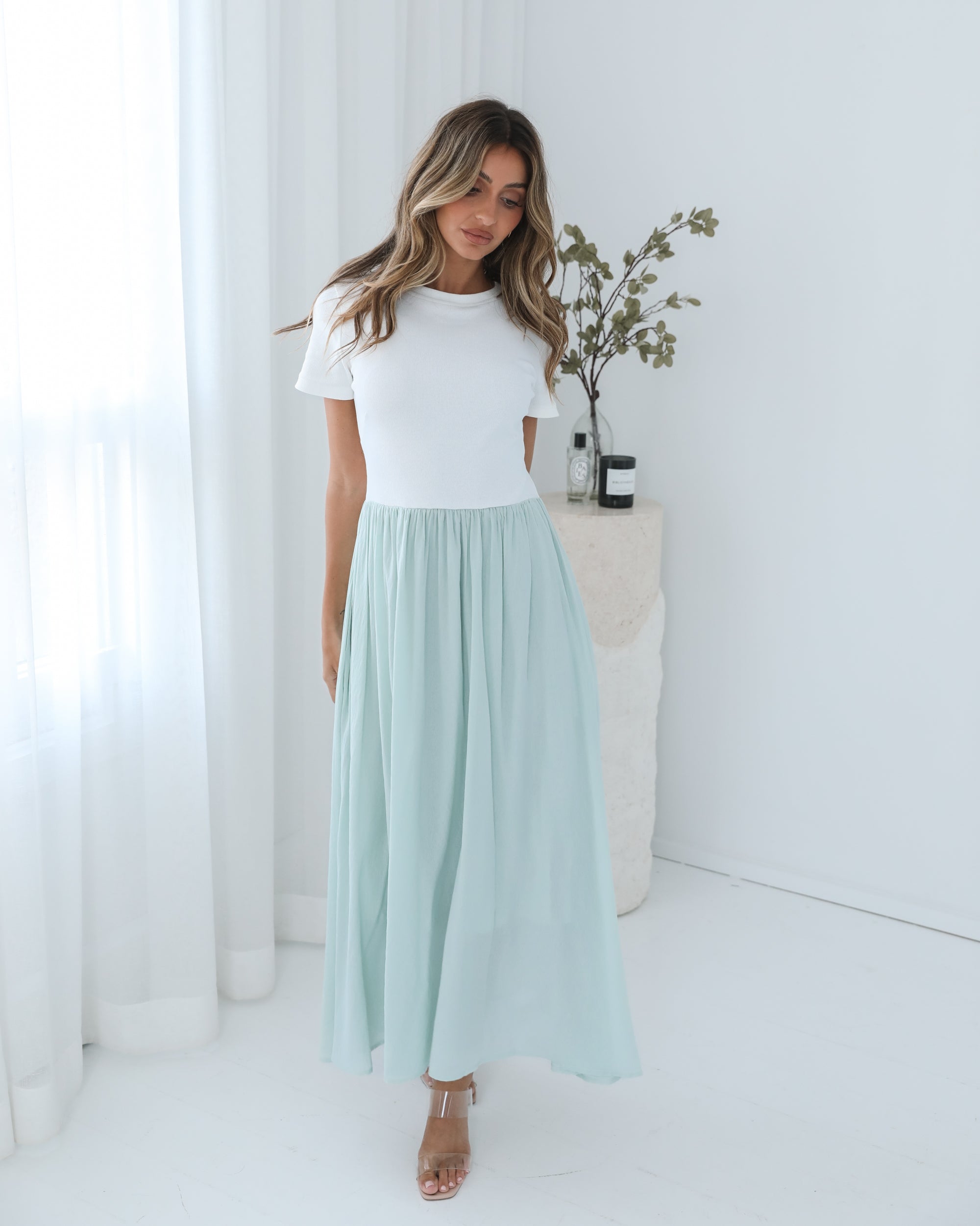 A woman wearing a knee-length dress with a round neckline and short sleeves. The dress is primarily white with sage green details.