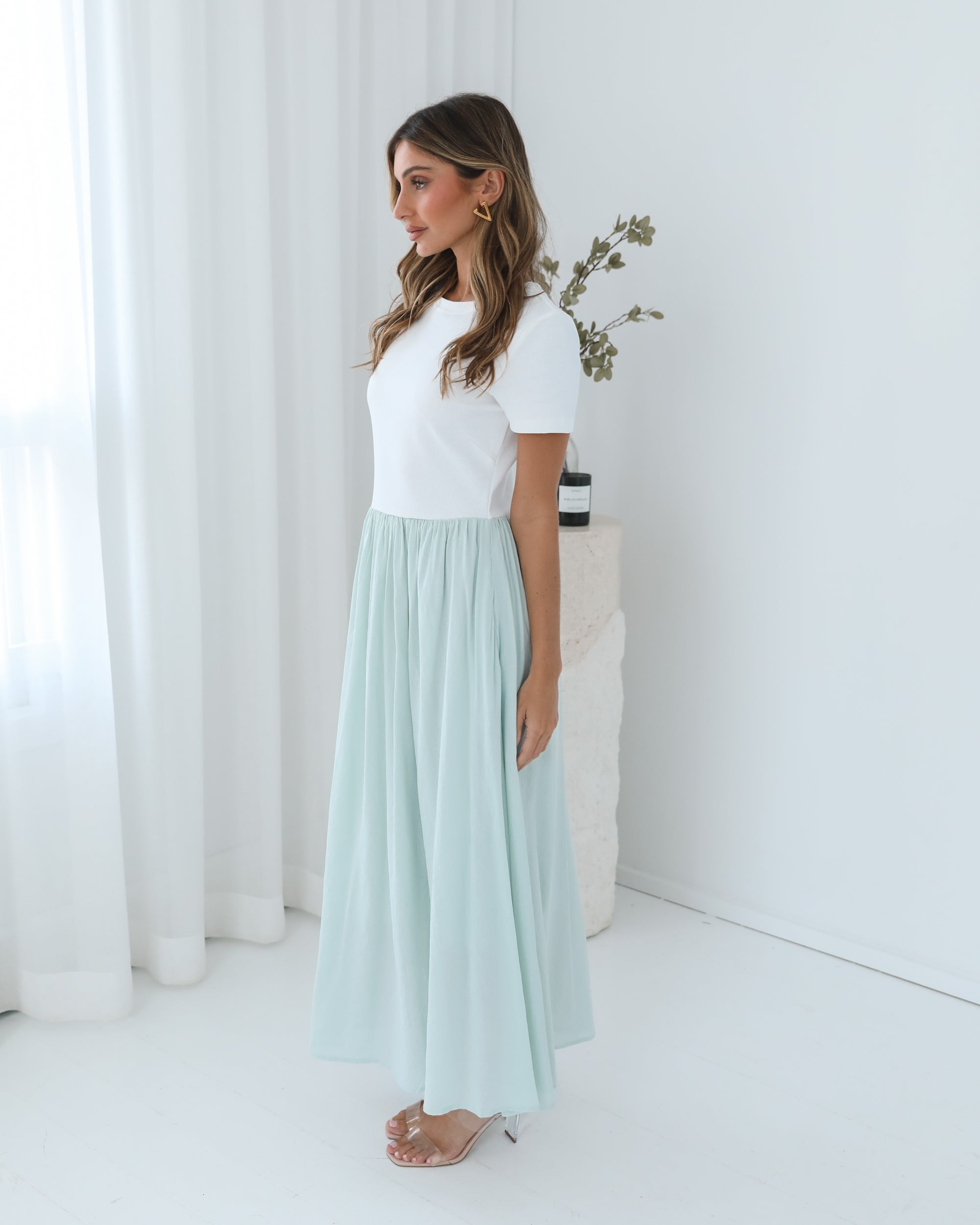 A woman wearing a knee-length dress with a round neckline and short sleeves. The dress is primarily white with sage green details.