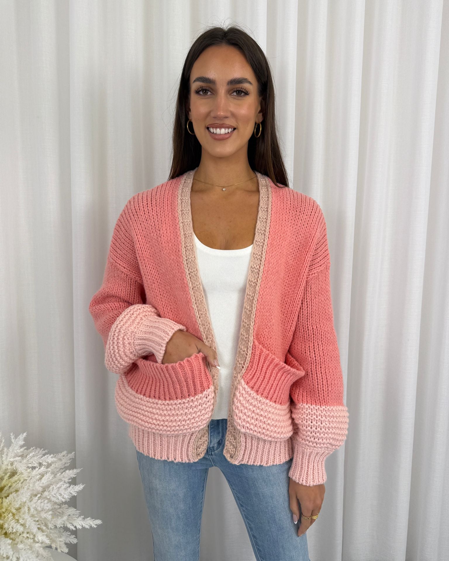 Woman wearing a pink knitted cardigan against a white curtain background