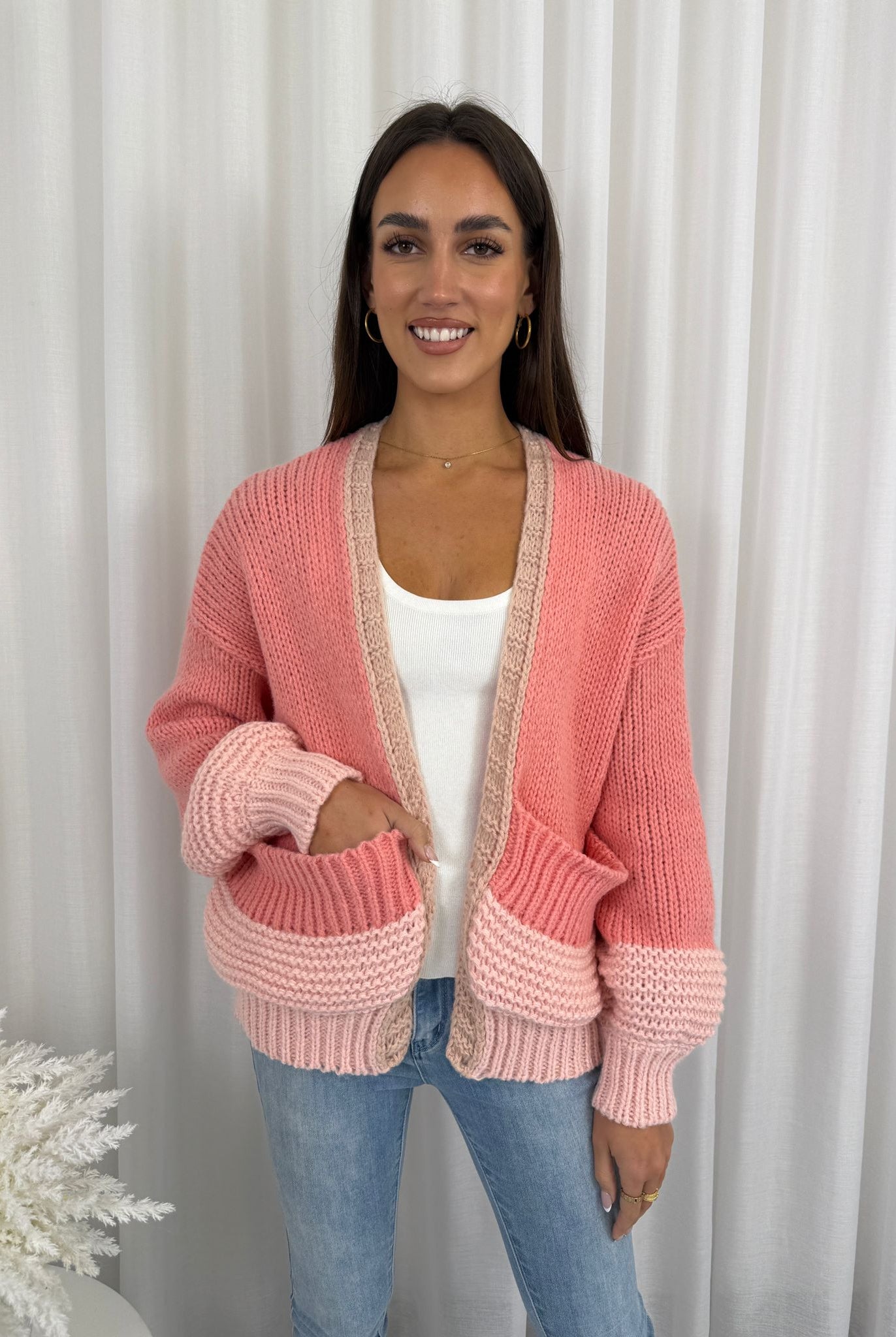 Woman wearing a pink knitted cardigan against a white curtain background