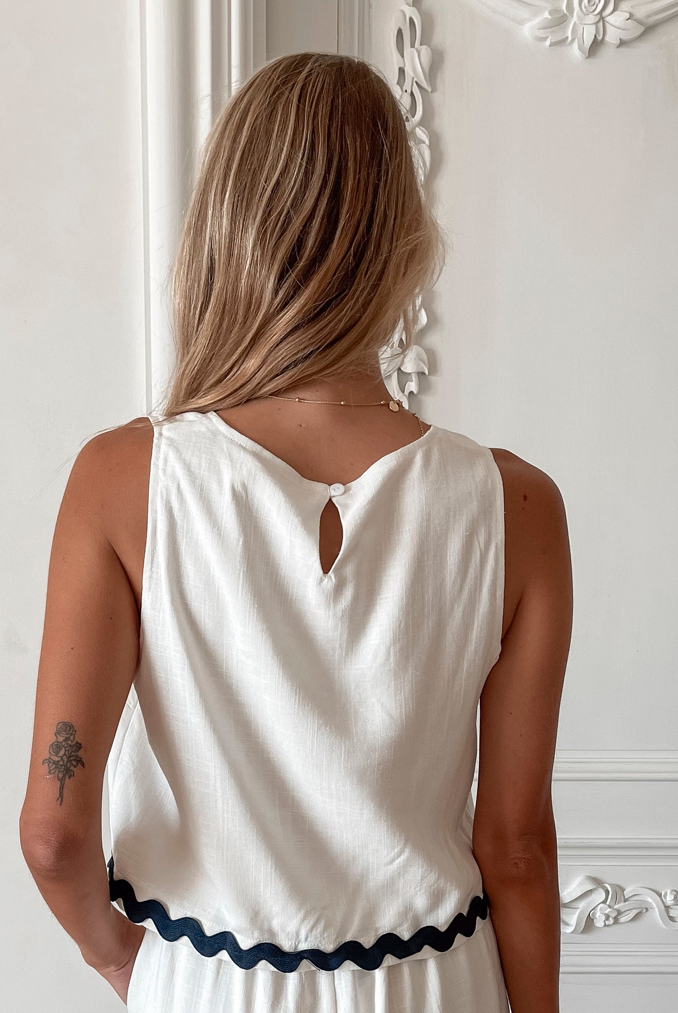 A woman wearing a white crop top with a square neckline and semi-relaxed fit, in a room with classic decor.