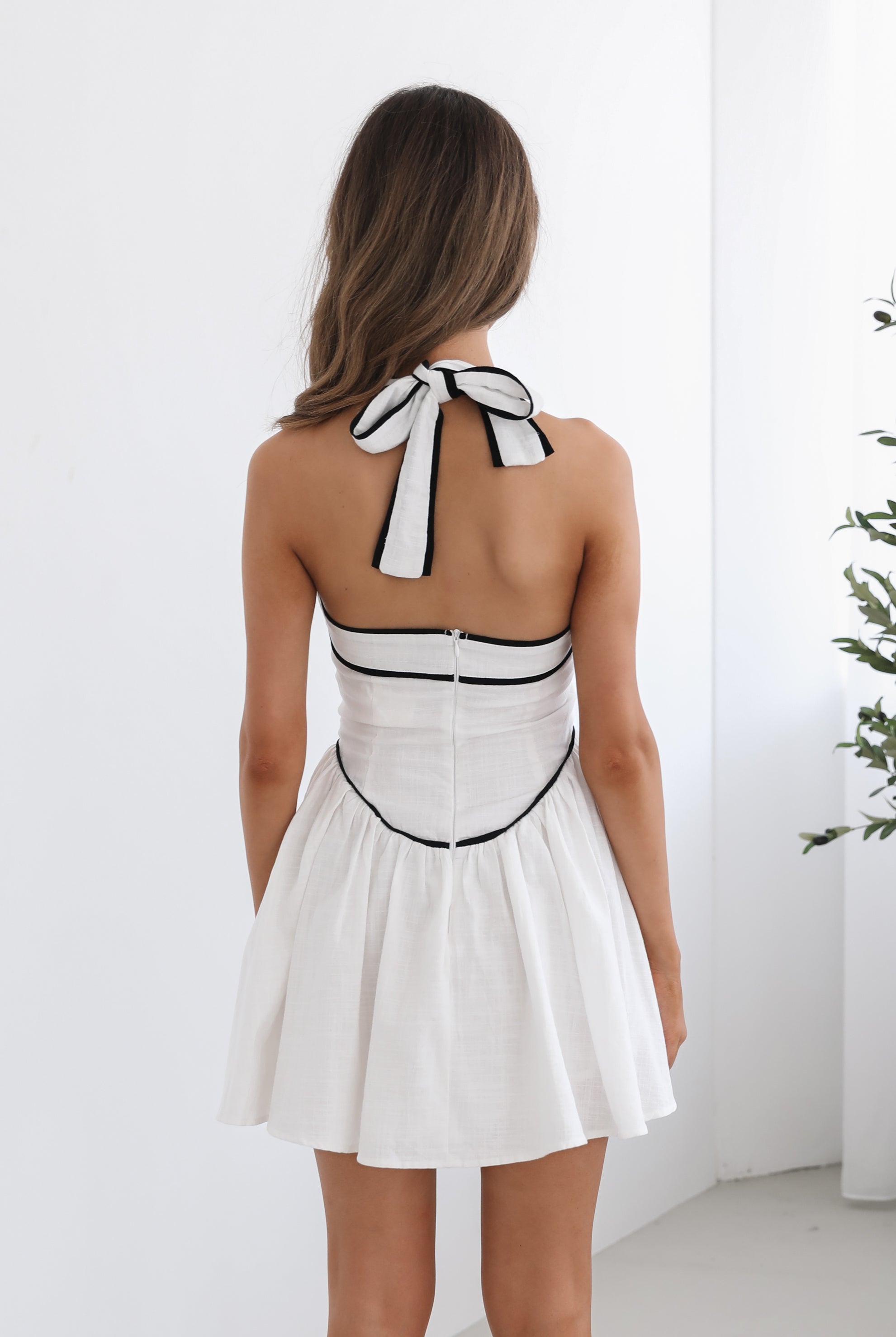 A woman wearing a white mini dress with a halter neck strap and contrasting black piping.