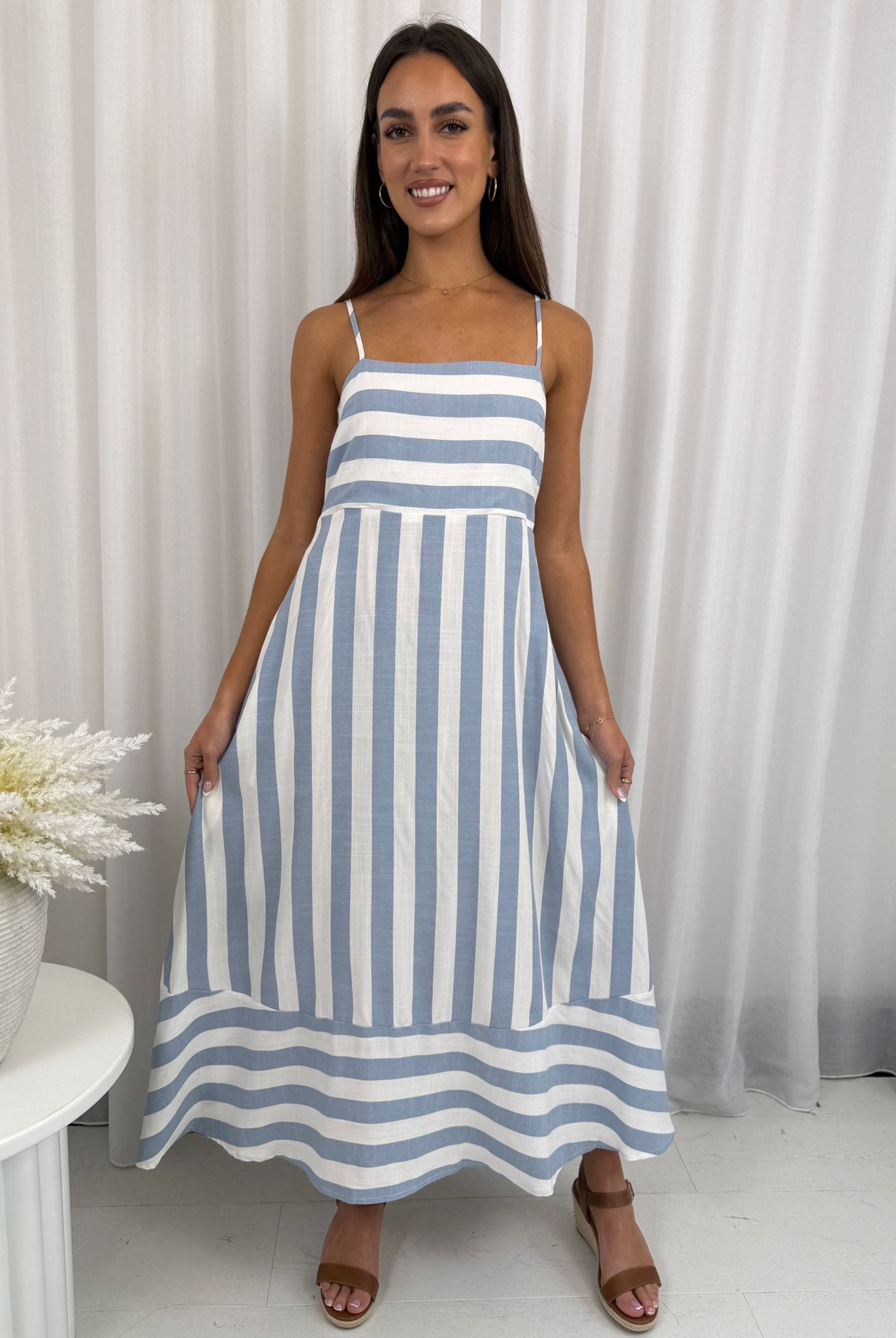 Woman wearing a blue and white striped dress against a white curtain background