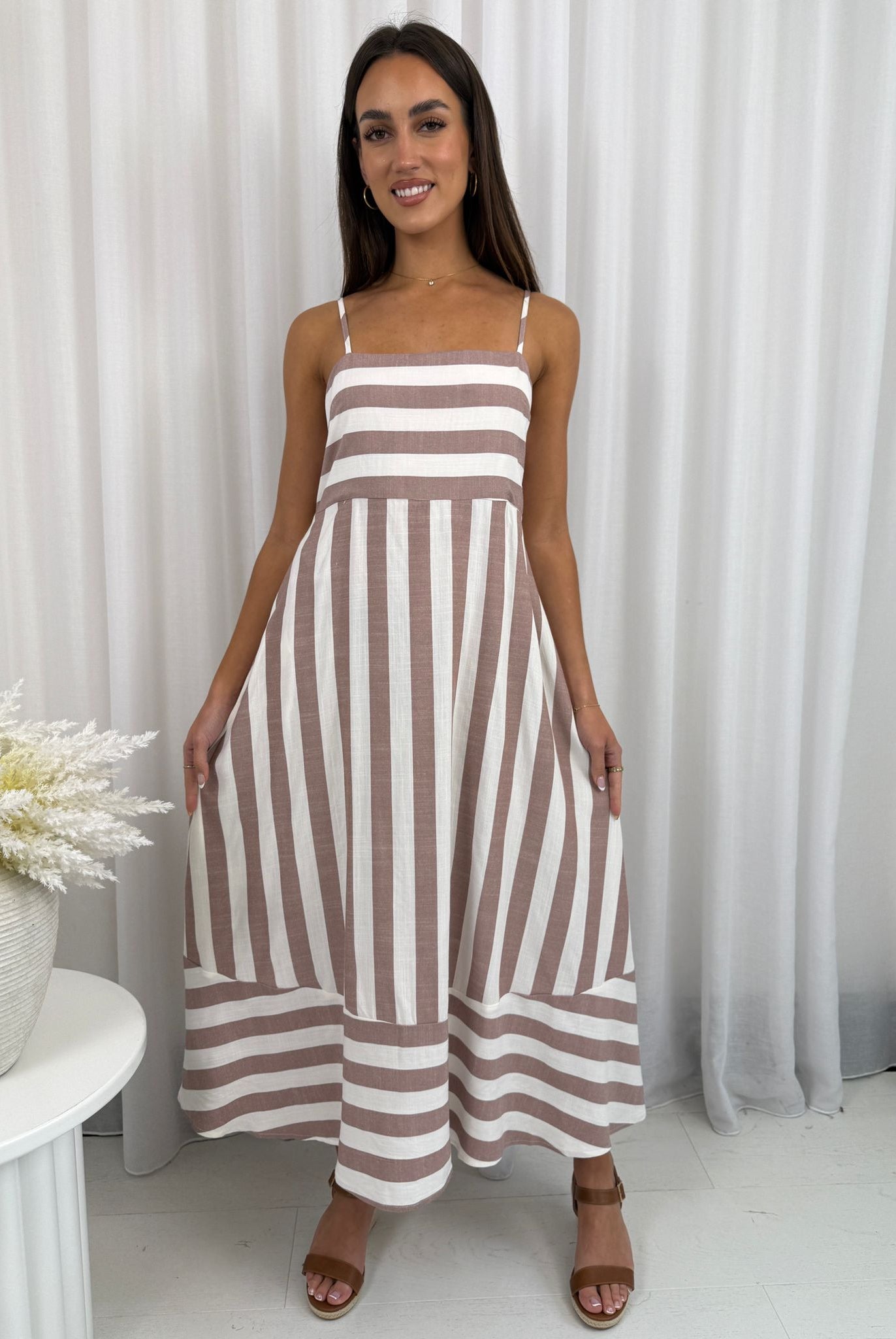 Woman wearing a brown and white striped dress against a white curtain background