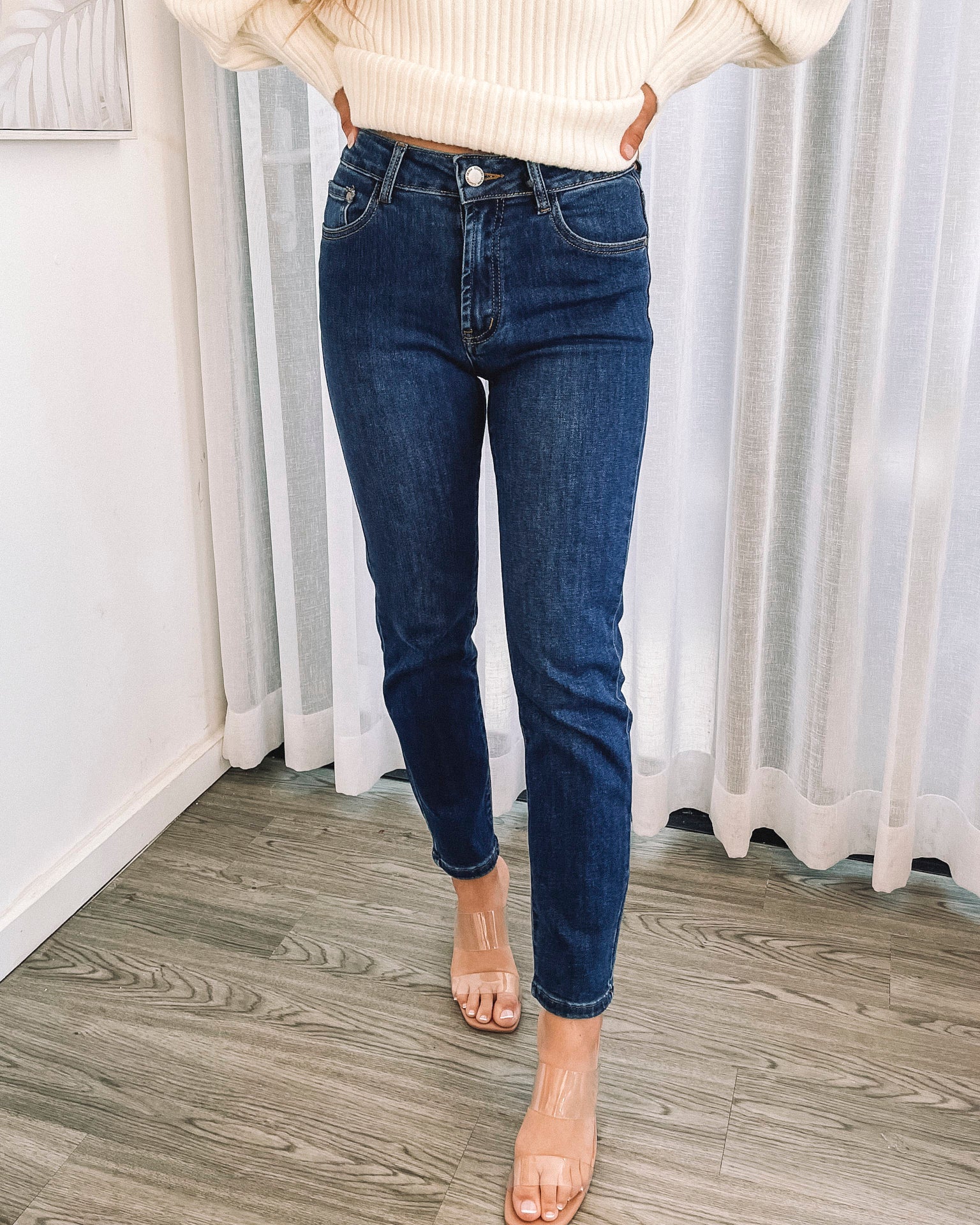 A person wearing a dark blue high-waisted, skinny fit pair of jeans with side pockets and a button and quarter zip closure.