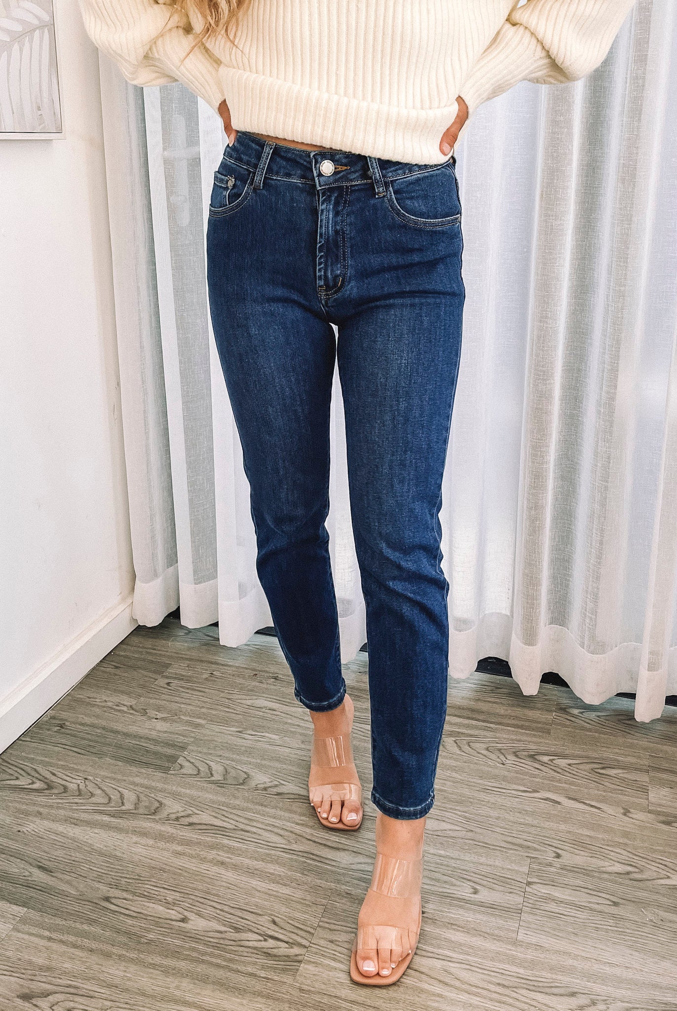 A person wearing a dark blue high-waisted, skinny fit pair of jeans with side pockets and a button and quarter zip closure.