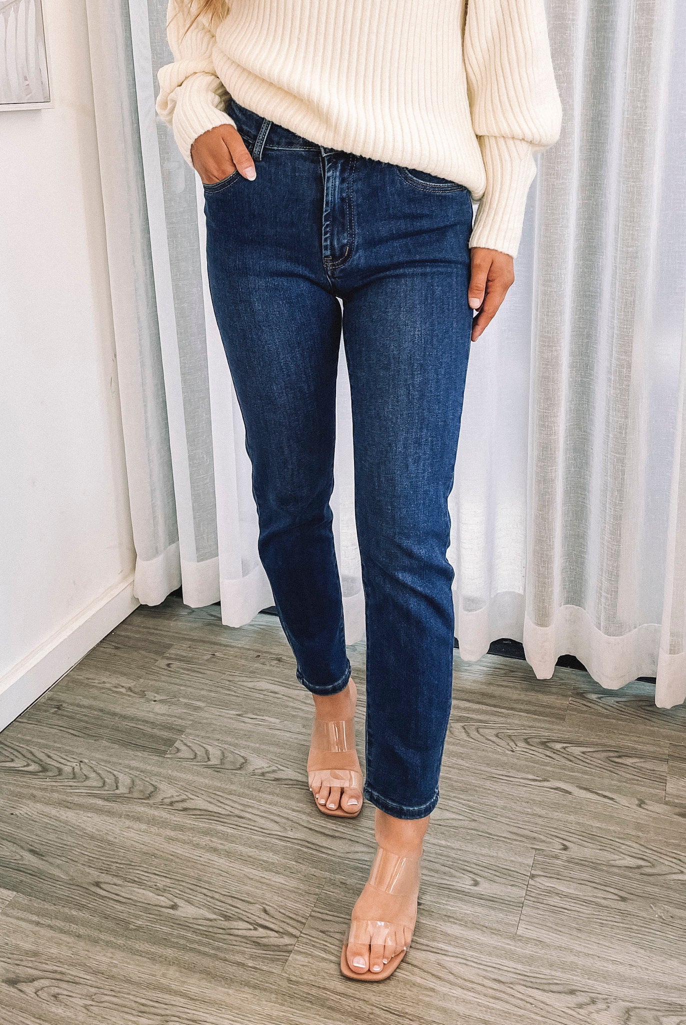 A person wearing a dark blue high-waisted, skinny fit pair of jeans with side pockets and a button and quarter zip closure.