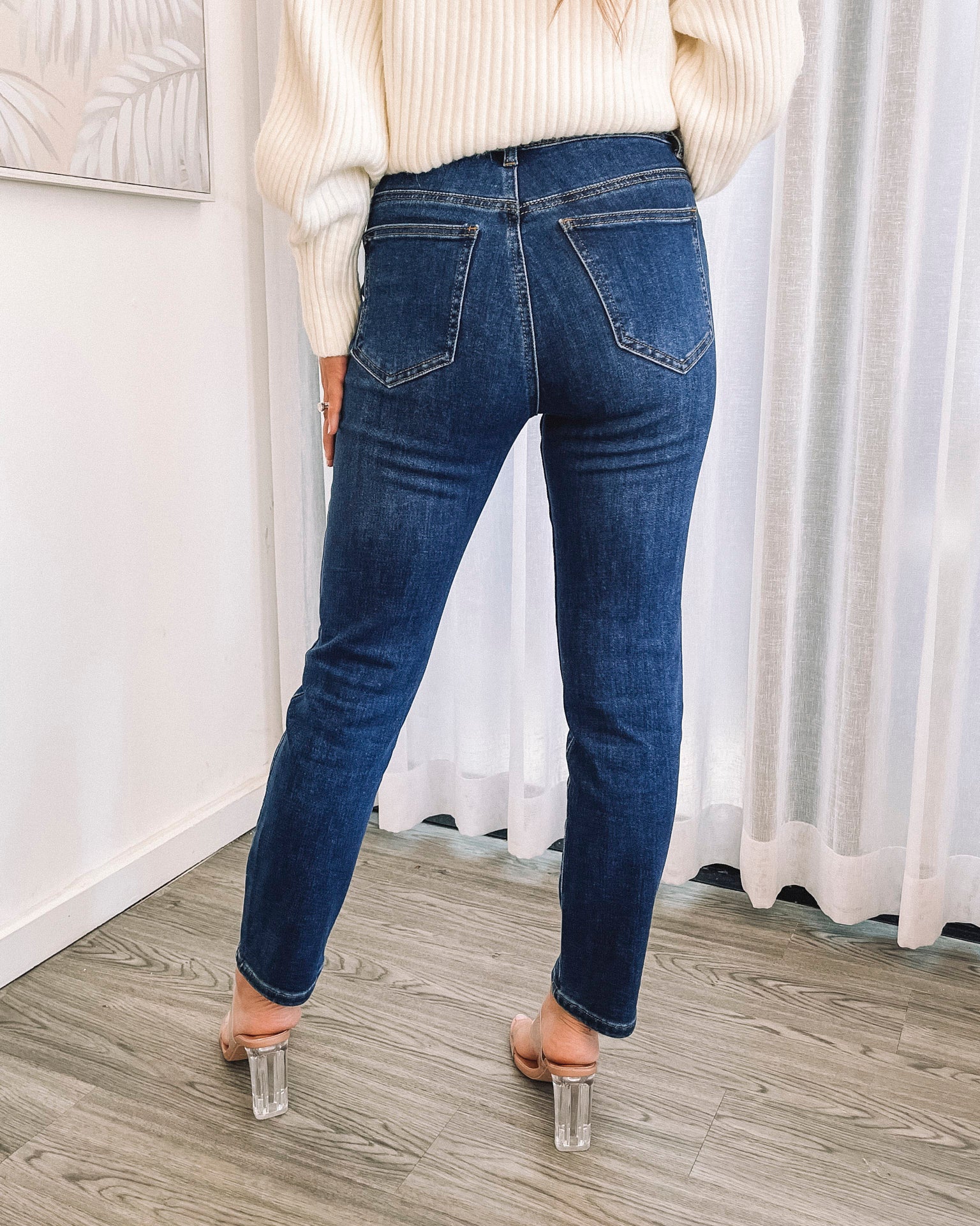 A person wearing a dark blue high-waisted, skinny fit pair of jeans with side pockets and a button and quarter zip closure.