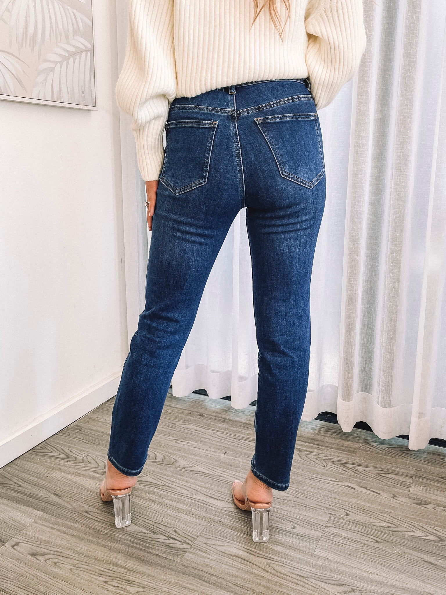 A person wearing a dark blue high-waisted, skinny fit pair of jeans with side pockets and a button and quarter zip closure.