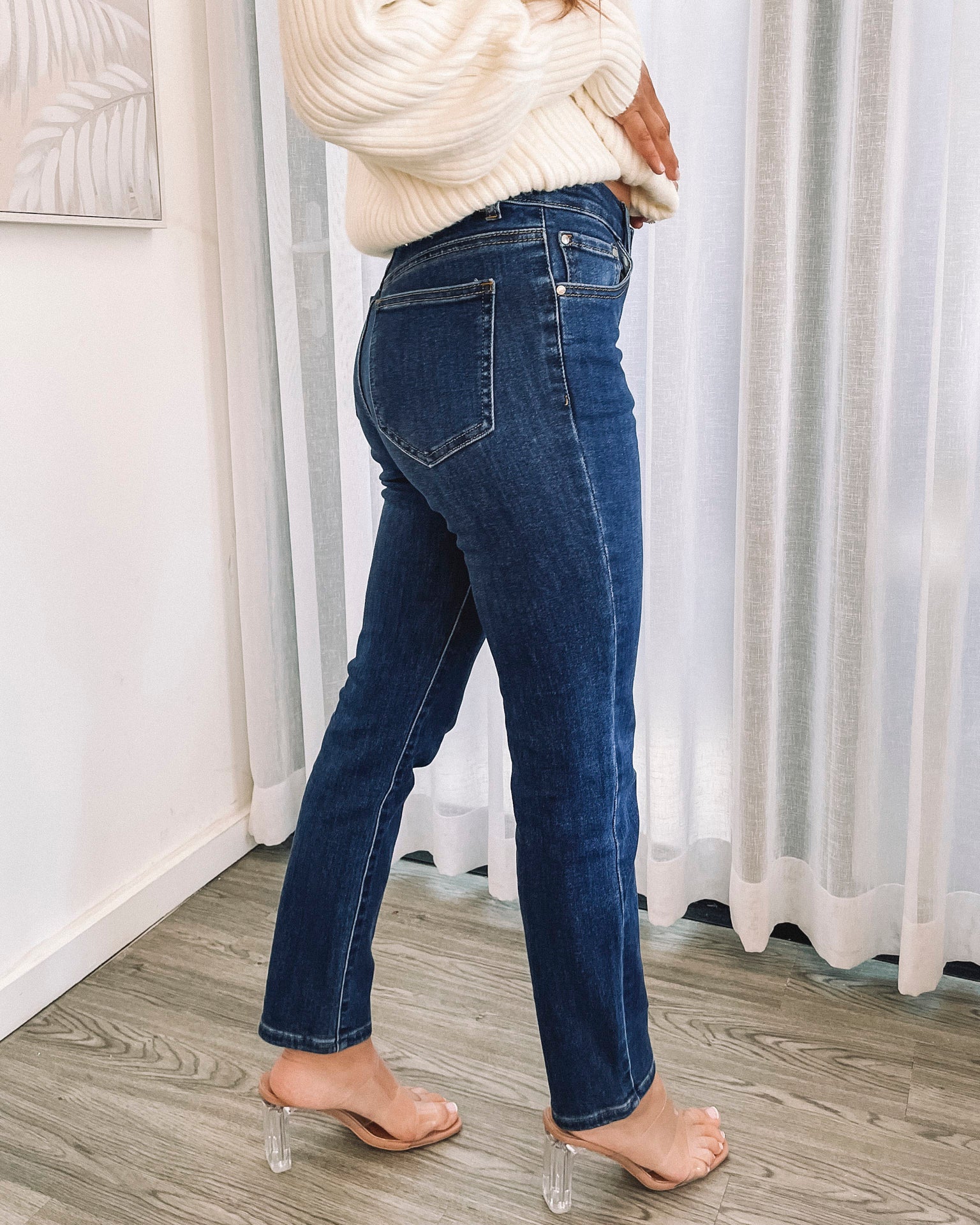 A person wearing a dark blue high-waisted, skinny fit pair of jeans with side pockets and a button and quarter zip closure.