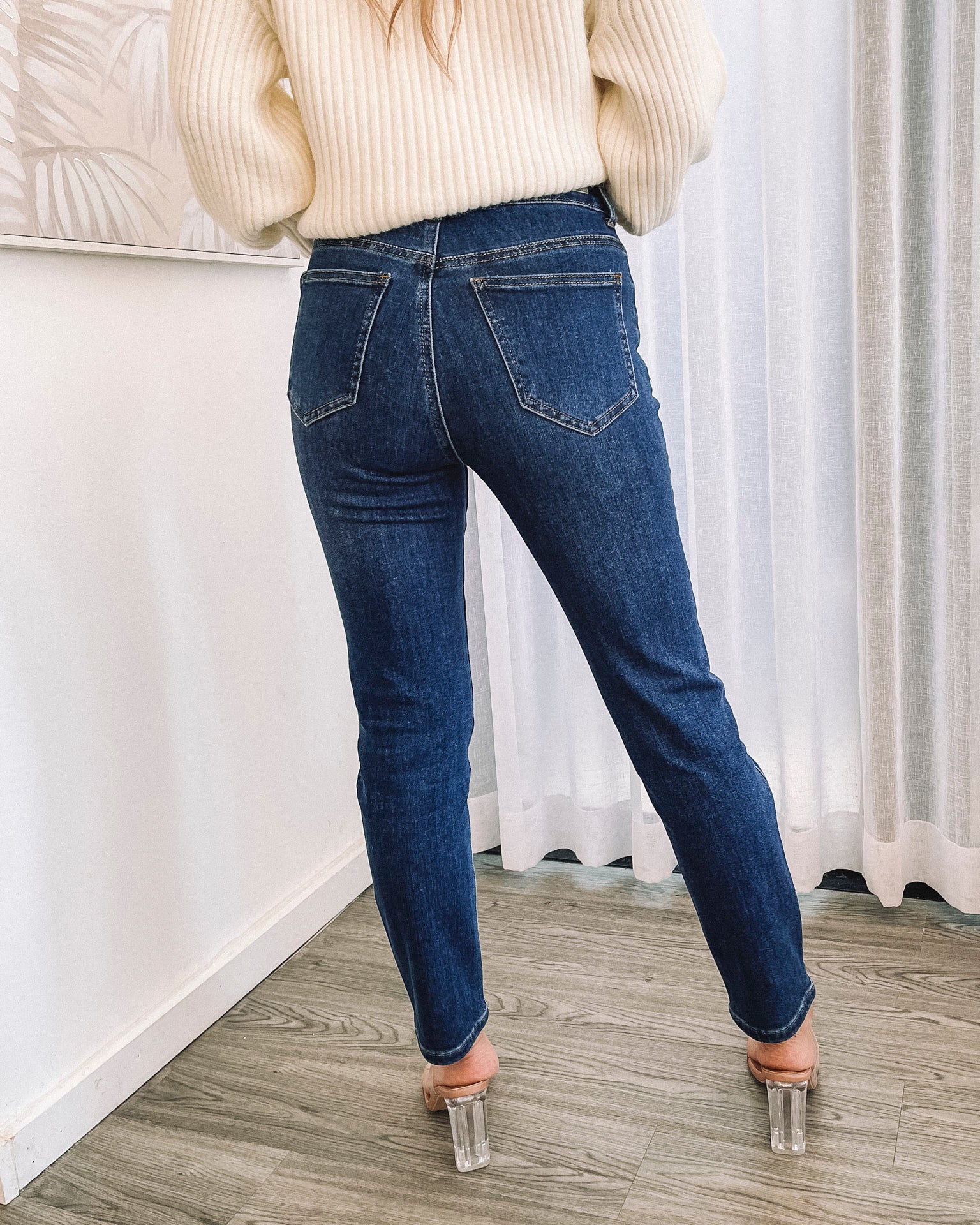 A person wearing a dark blue high-waisted, skinny fit pair of jeans with side pockets and a button and quarter zip closure.