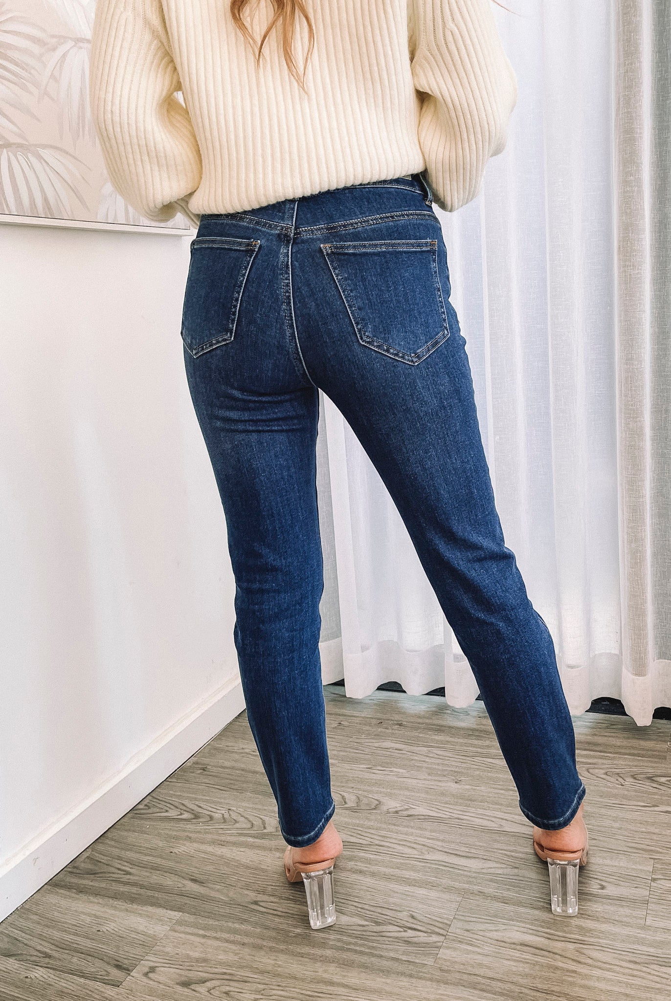 A person wearing a dark blue high-waisted, skinny fit pair of jeans with side pockets and a button and quarter zip closure.