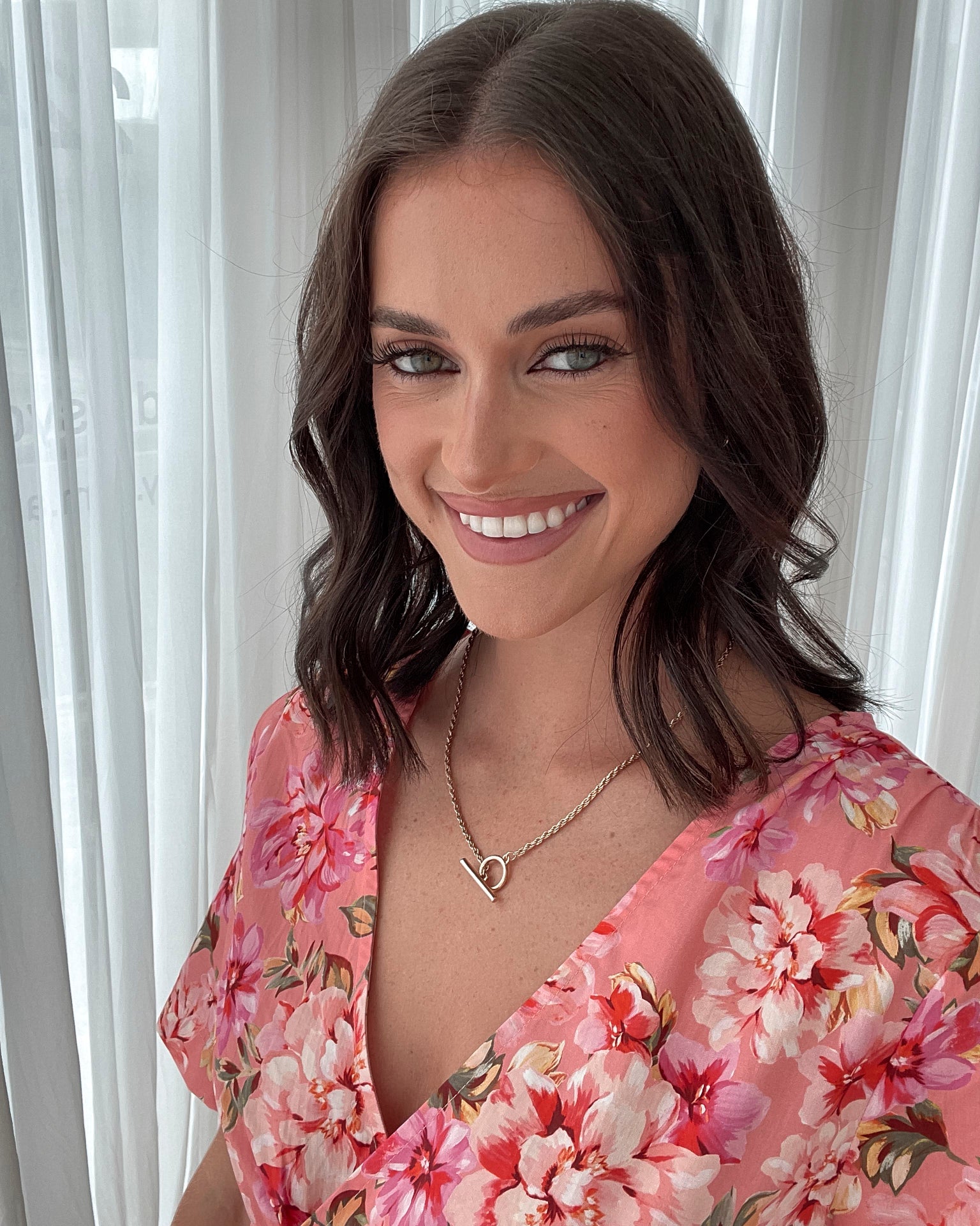 A person sitting on a white sofa wearing a peach blossom midi dress with a wide v-neckline, short puff sleeves, and a flowy a-line skirt.