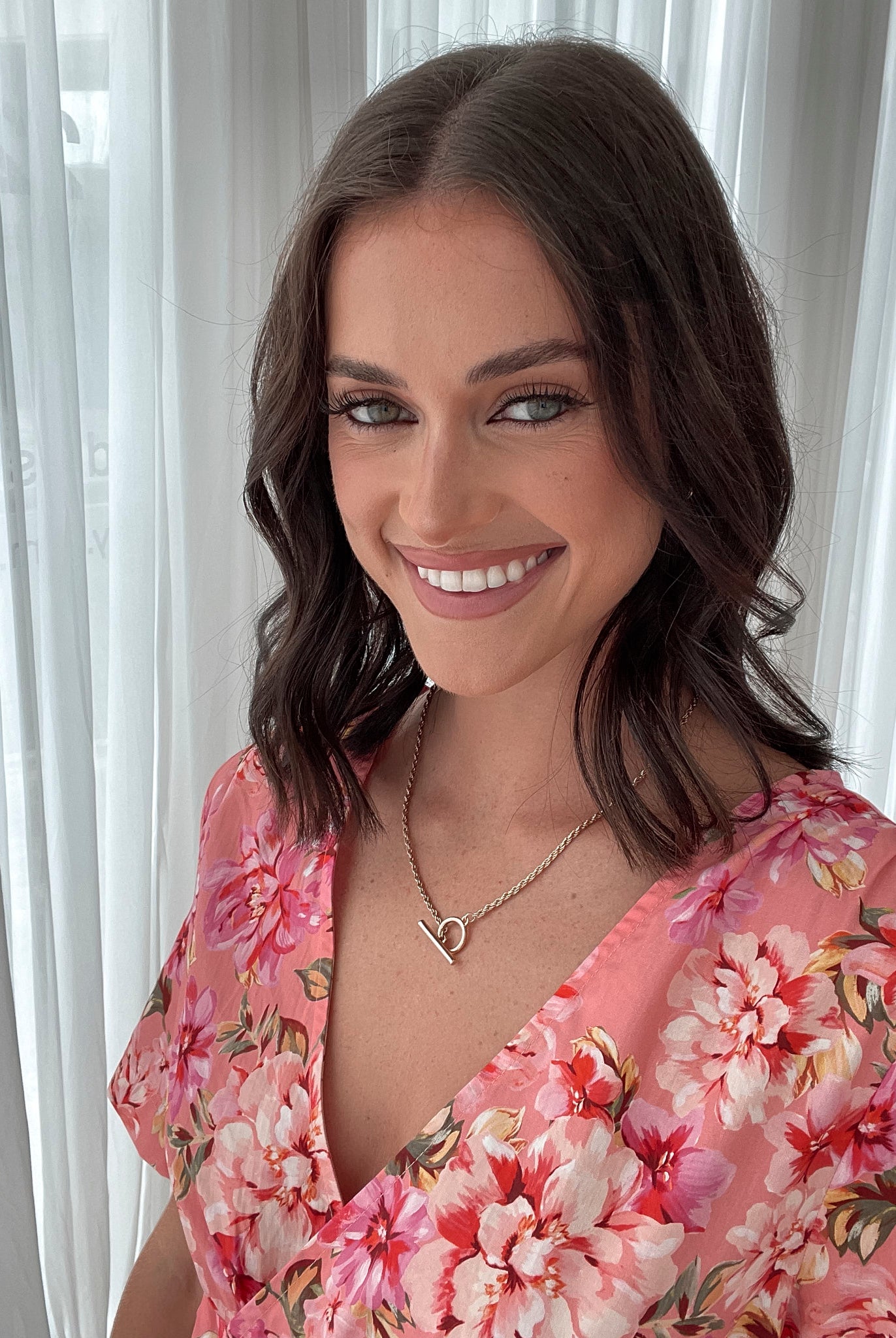 A person sitting on a white sofa wearing a peach blossom midi dress with a wide v-neckline, short puff sleeves, and a flowy a-line skirt.