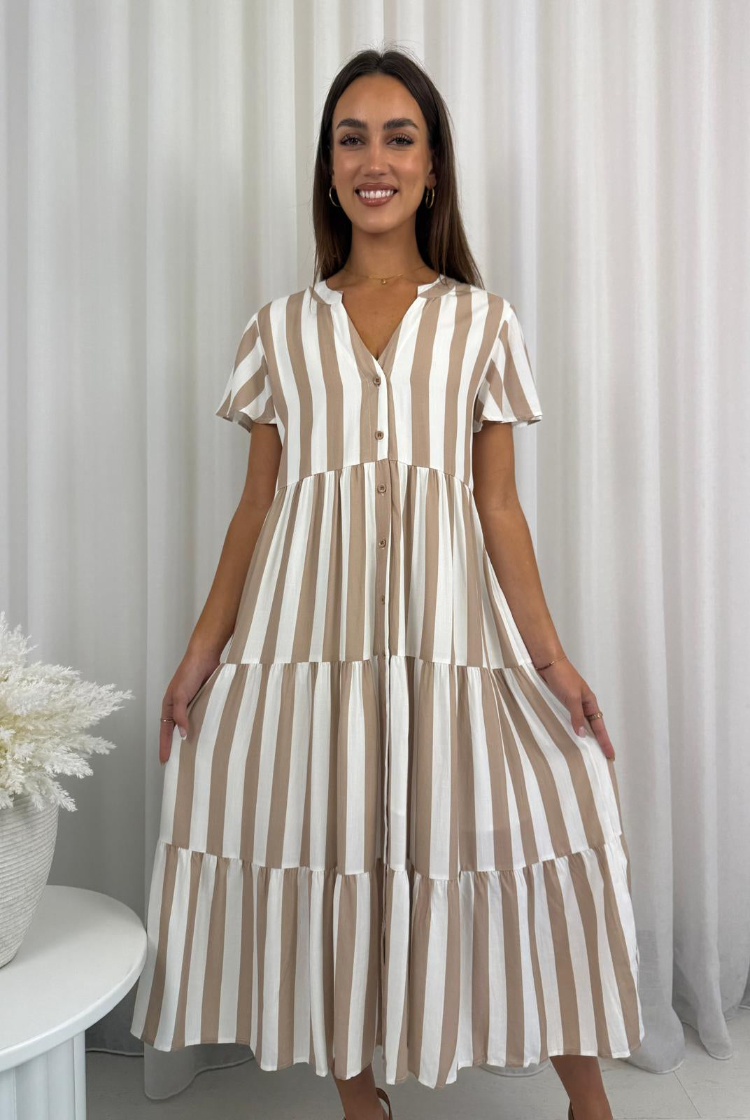 Woman wearing a brown and white striped dress against a white curtain background