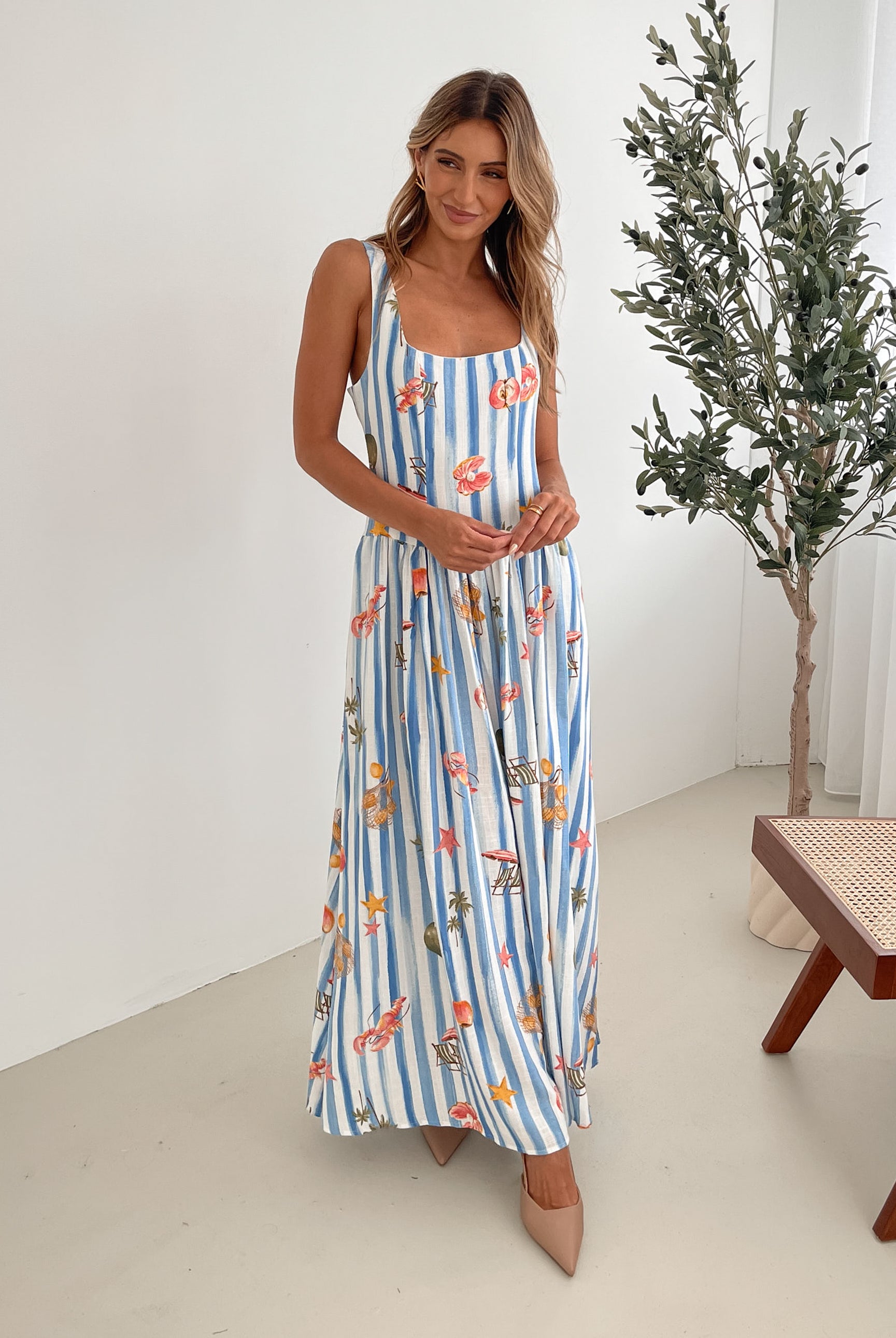A model wearing a white and blue base multicolored print maxi dress with a square neckline and wide straps.