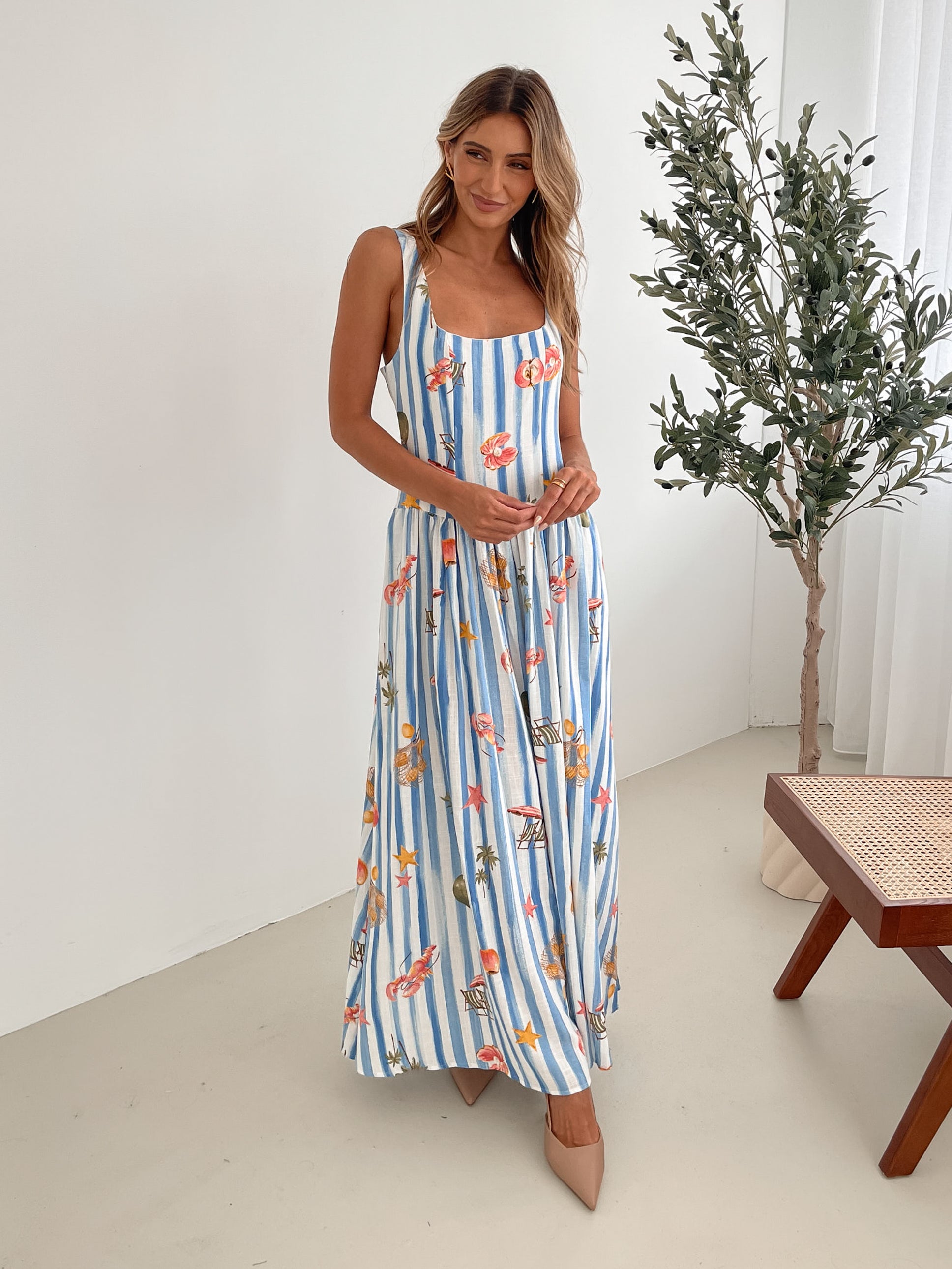 A model wearing a white and blue base multicolored print maxi dress with a square neckline and wide straps.