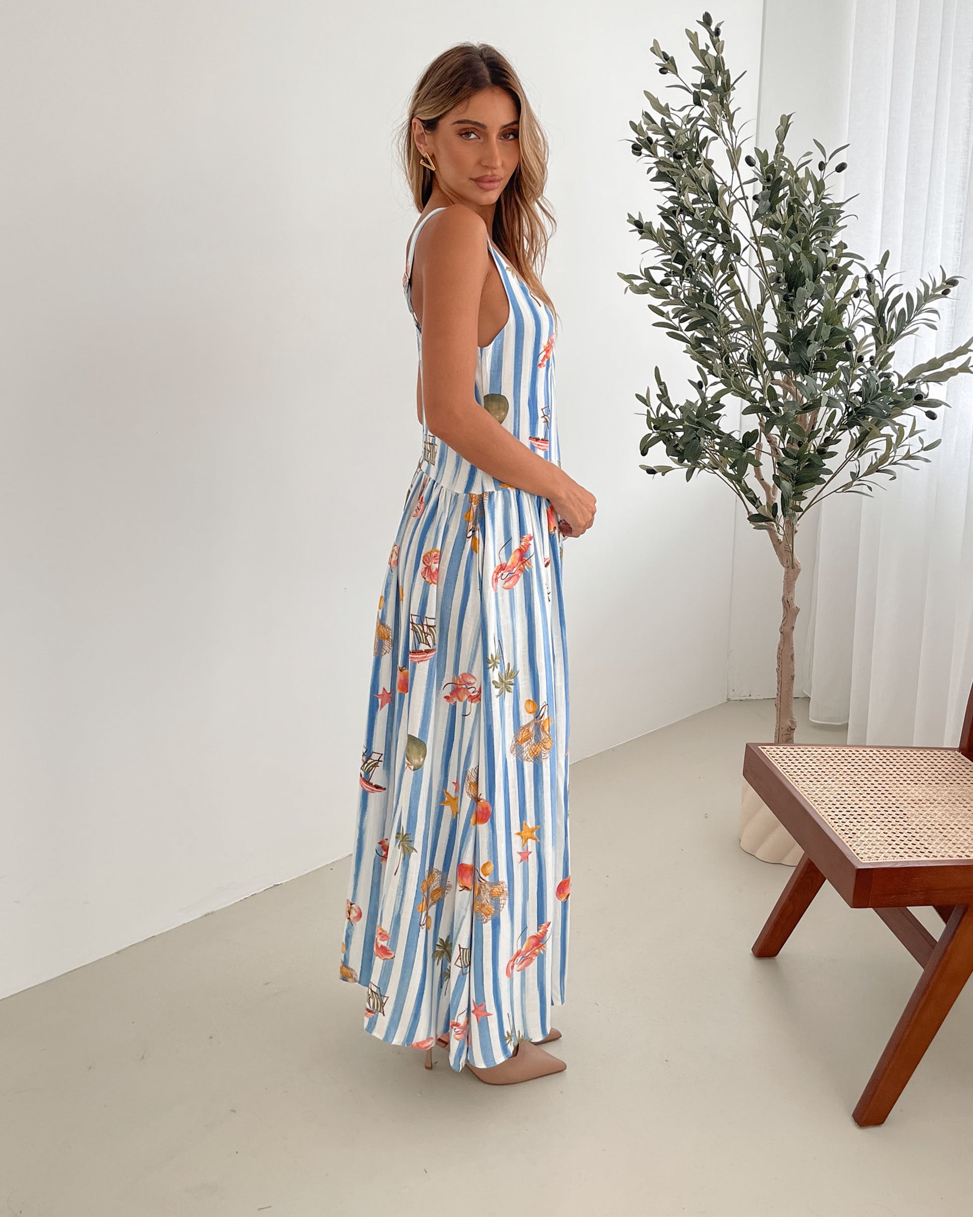A model wearing a white and blue base multicolored print maxi dress with a square neckline and wide straps.
