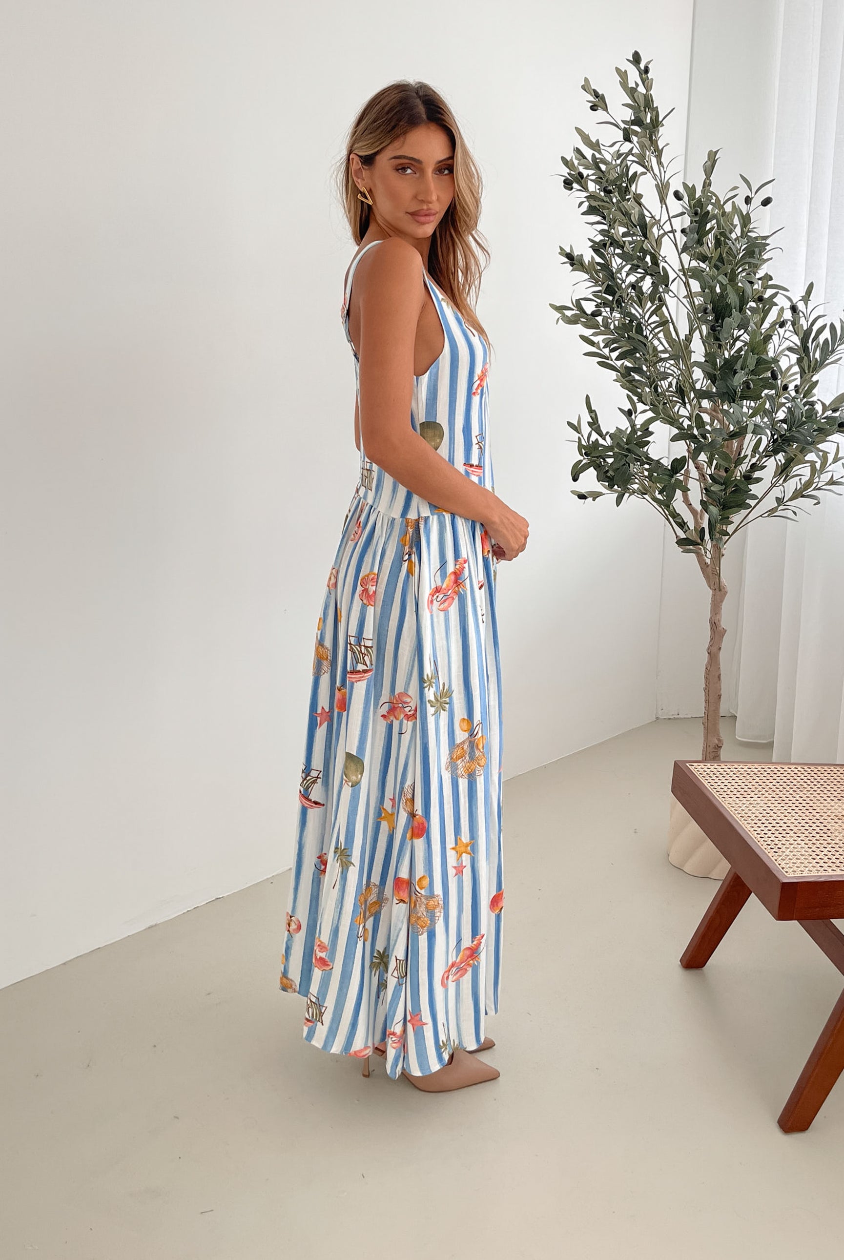 A model wearing a white and blue base multicolored print maxi dress with a square neckline and wide straps.
