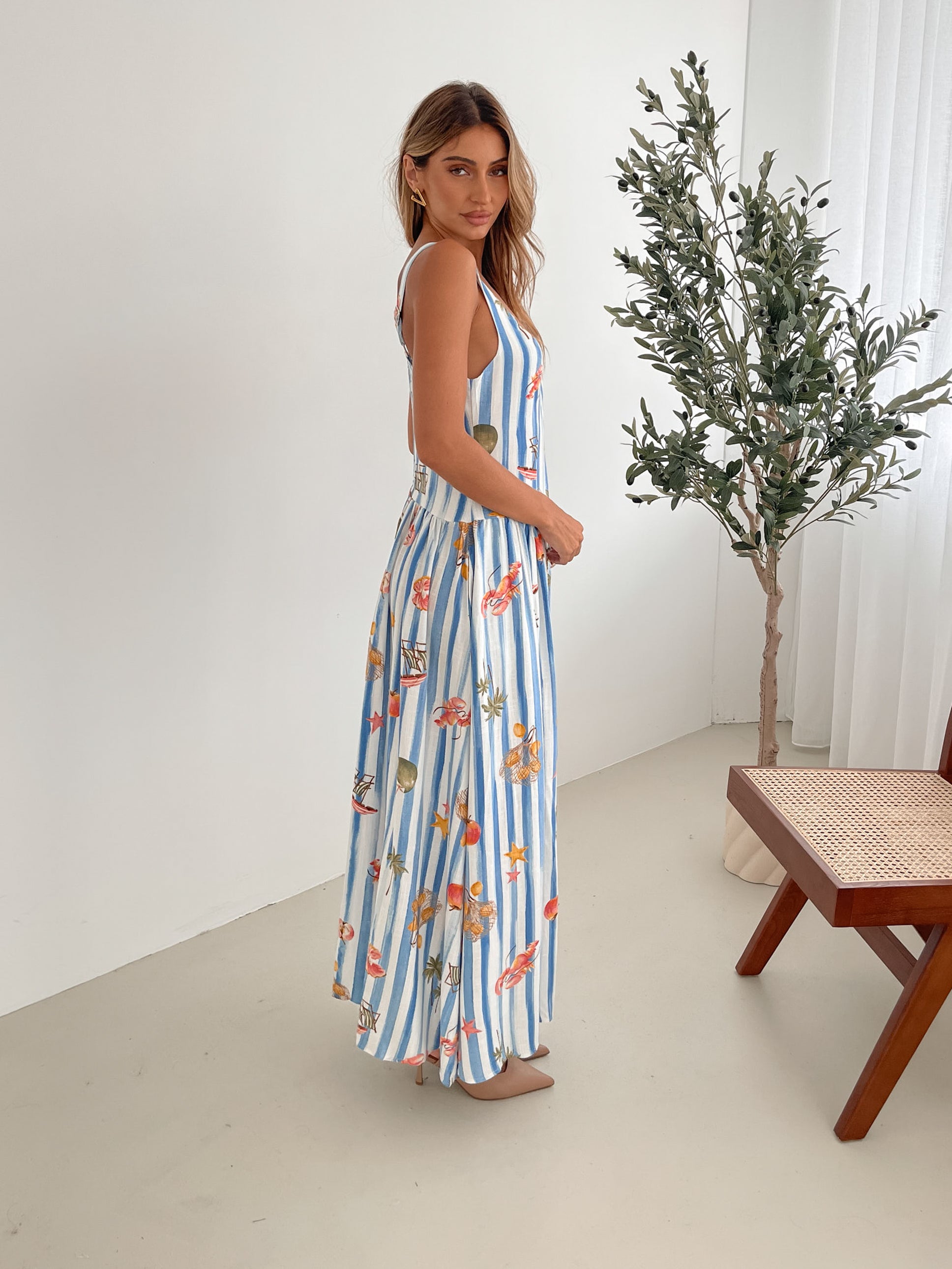 A model wearing a white and blue base multicolored print maxi dress with a square neckline and wide straps.