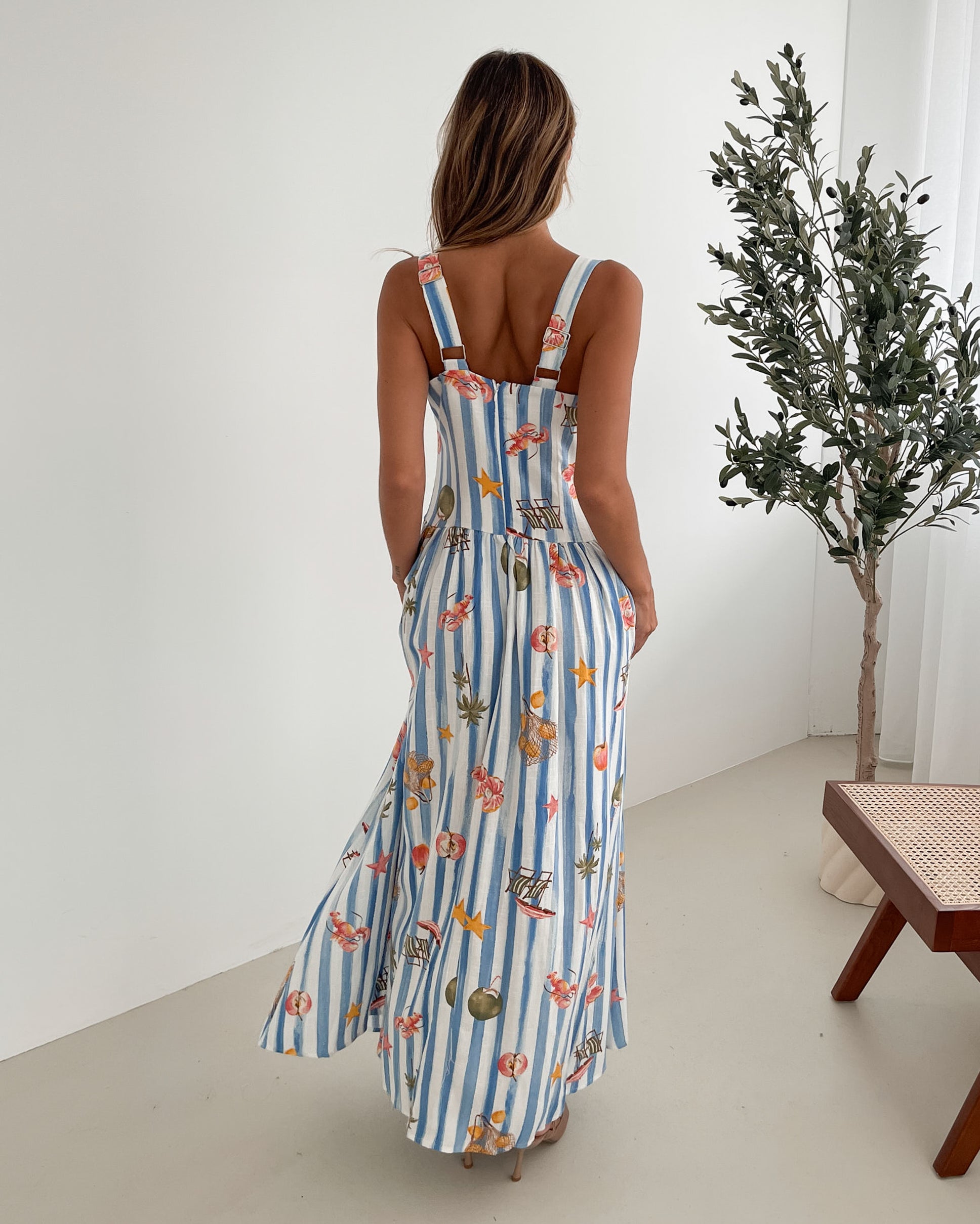 A model wearing a white and blue base multicolored print maxi dress with a square neckline and wide straps.