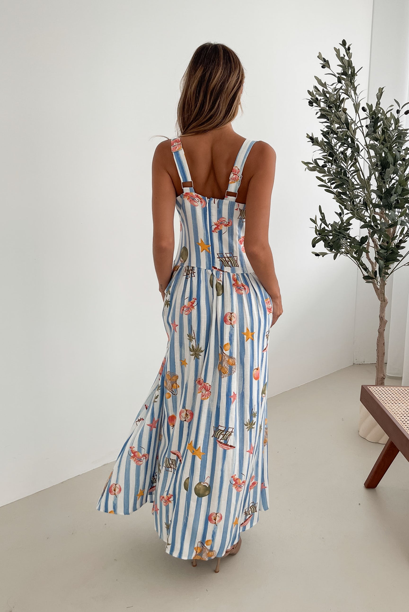 A model wearing a white and blue base multicolored print maxi dress with a square neckline and wide straps.