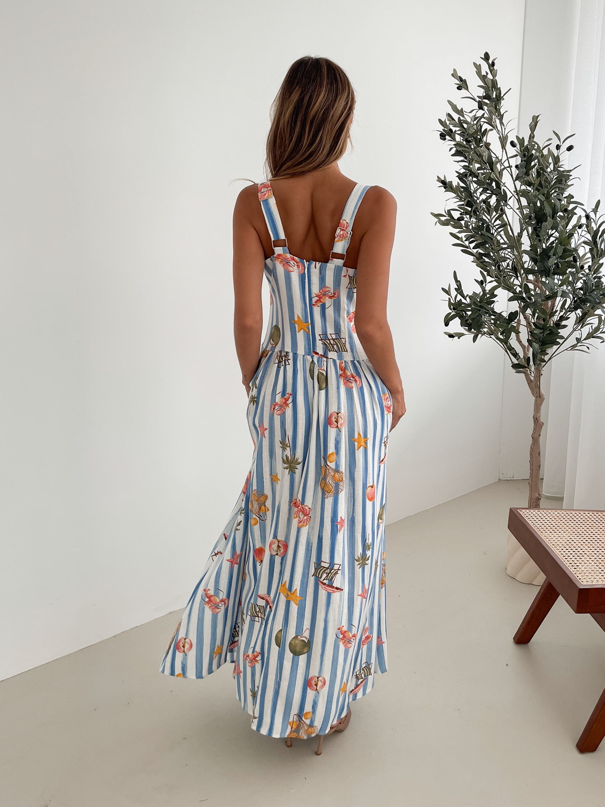 A model wearing a white and blue base multicolored print maxi dress with a square neckline and wide straps.