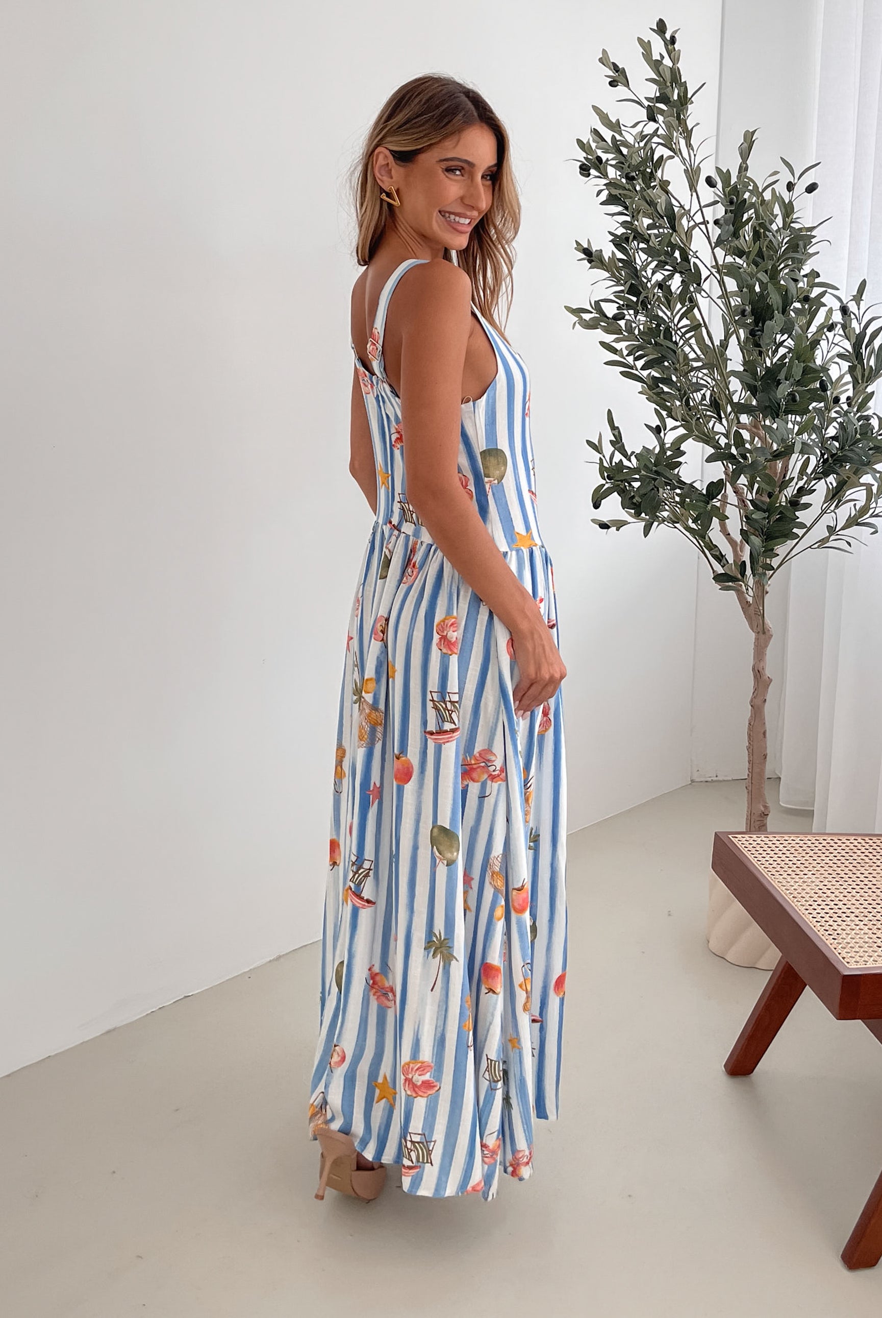 A model wearing a white and blue base multicolored print maxi dress with a square neckline and wide straps.