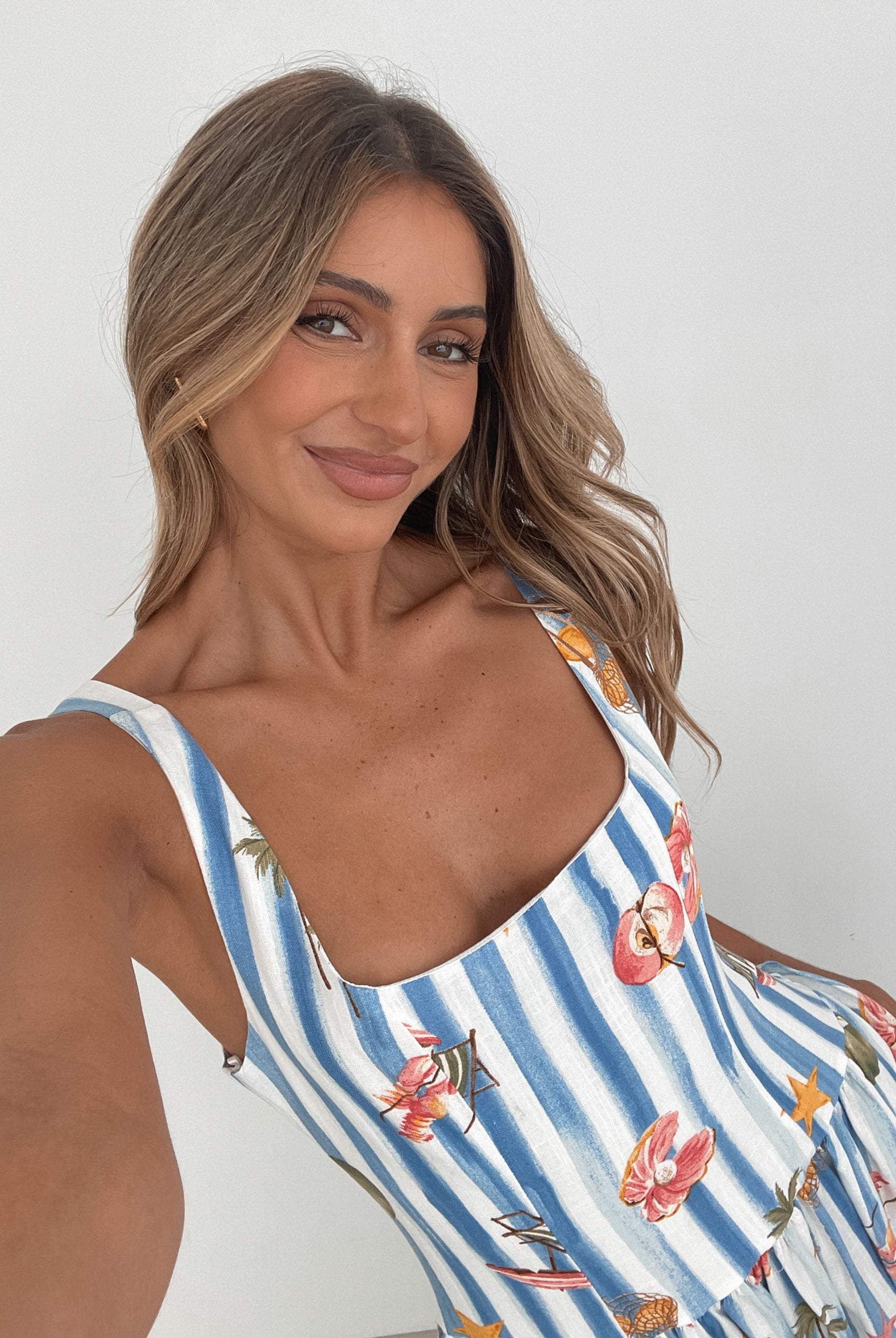 A model wearing a white and blue base multicolored print maxi dress with a square neckline and wide straps.