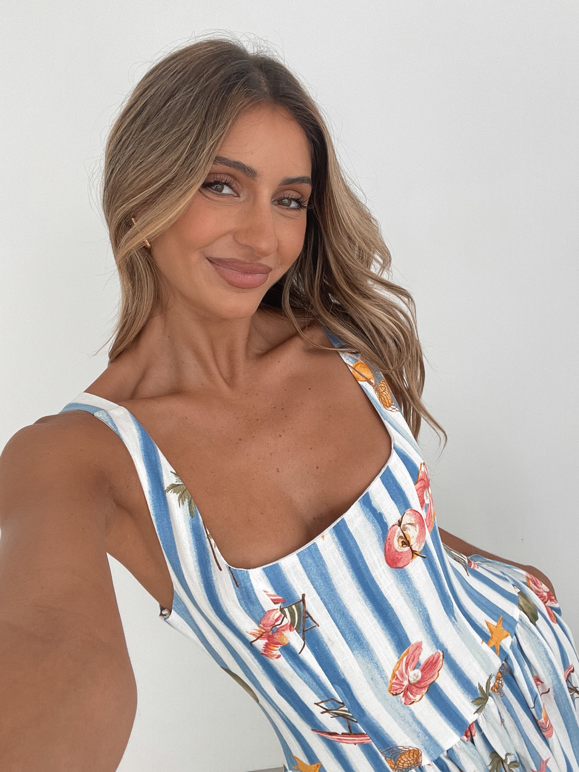 A model wearing a white and blue base multicolored print maxi dress with a square neckline and wide straps.