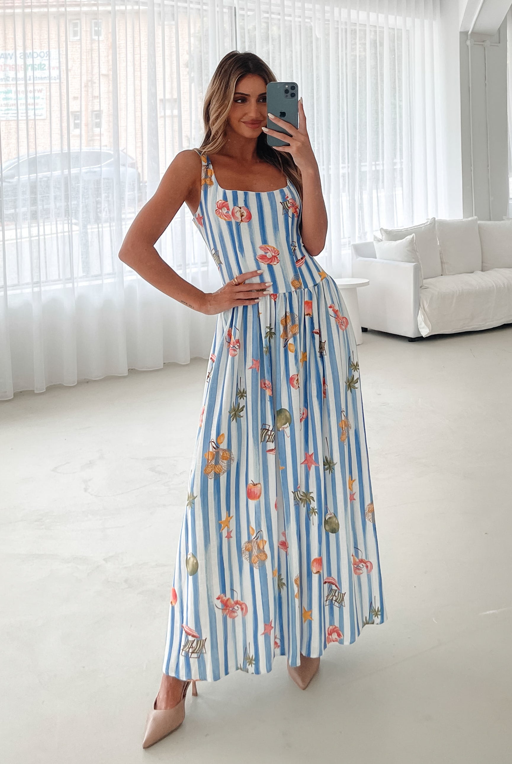 A model wearing a white and blue base multicolored print maxi dress with a square neckline and wide straps.