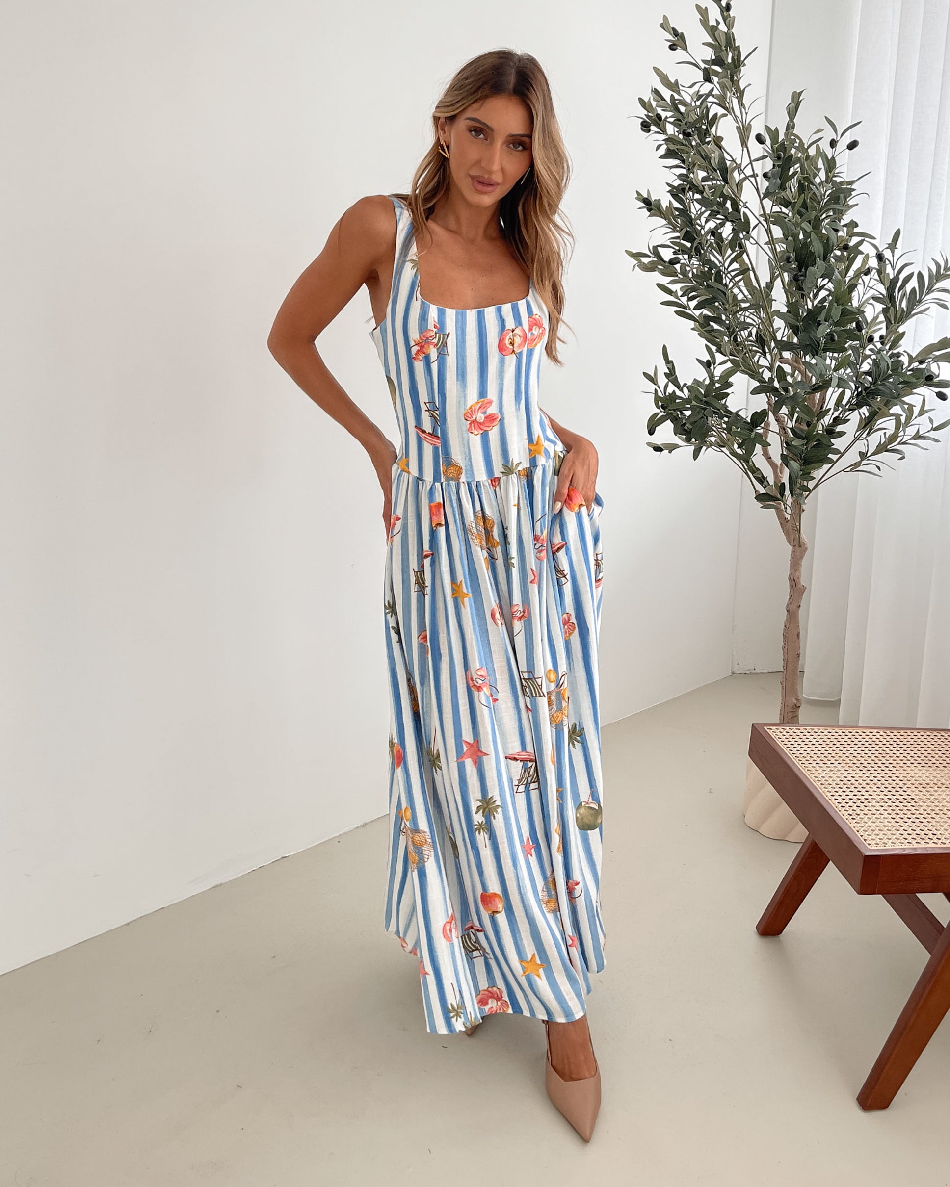 A model wearing a white and blue base multicolored print maxi dress with a square neckline and wide straps.