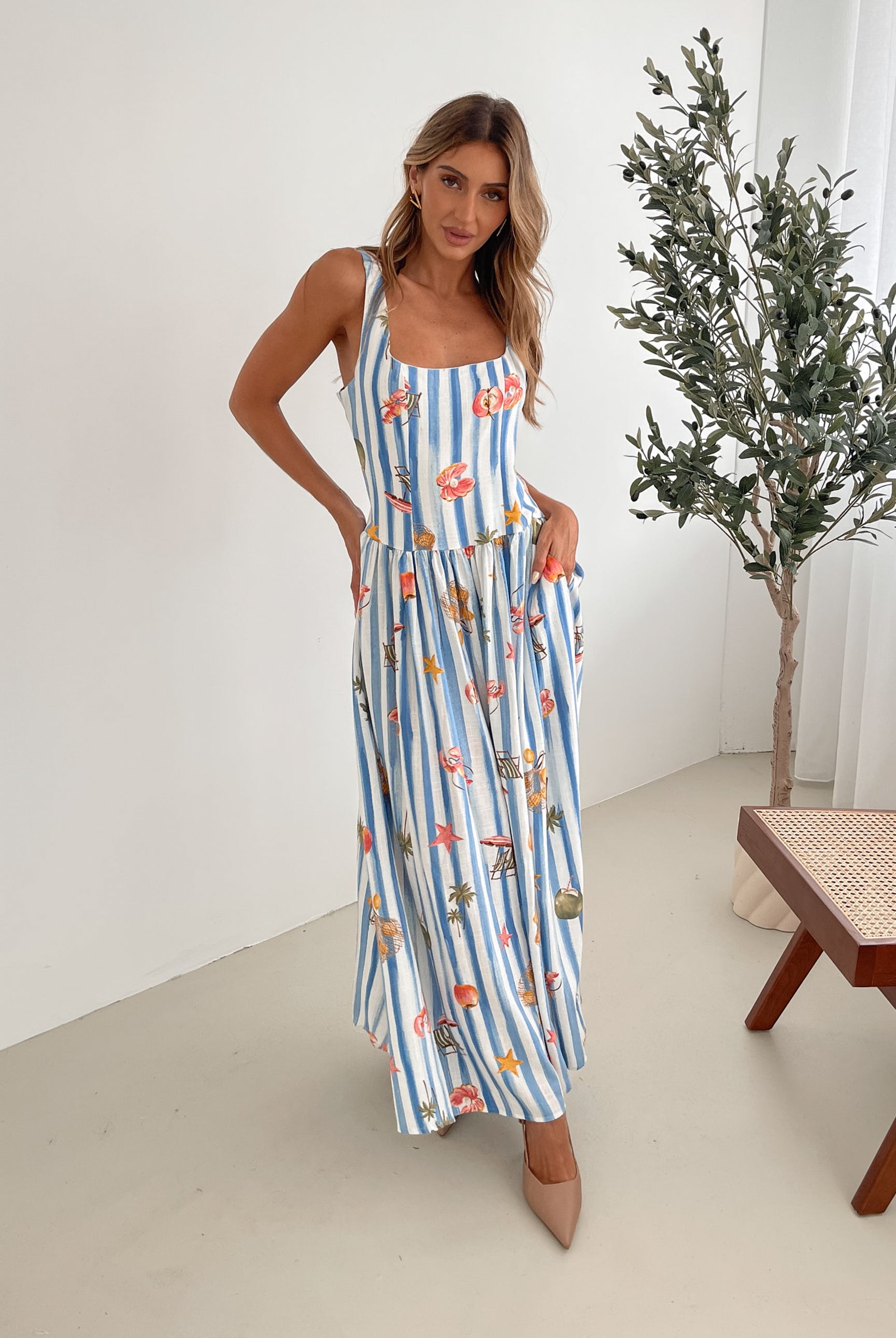 A model wearing a white and blue base multicolored print maxi dress with a square neckline and wide straps.