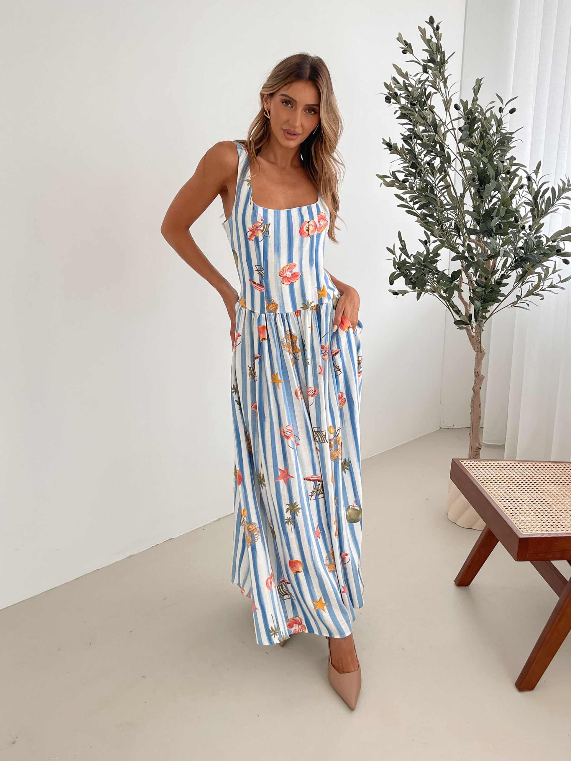 A model wearing a white and blue base multicolored print maxi dress with a square neckline and wide straps.