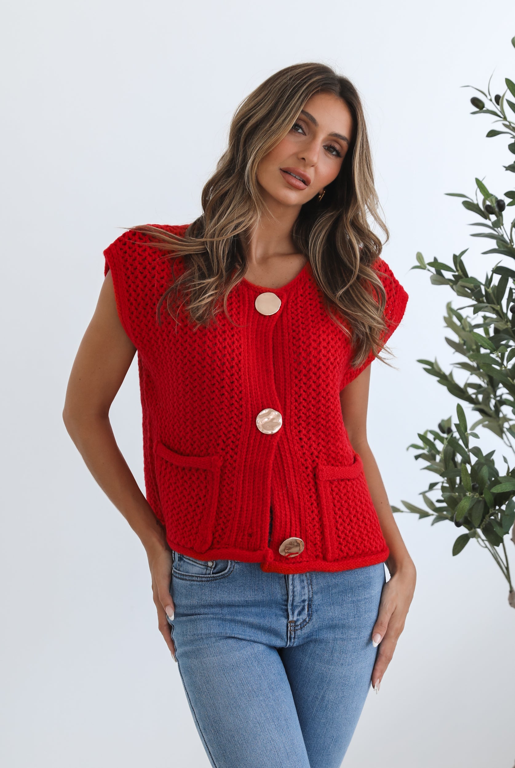 A woman wearing a red knit top with round neckline and center-front buttons, paired with blue jeans.