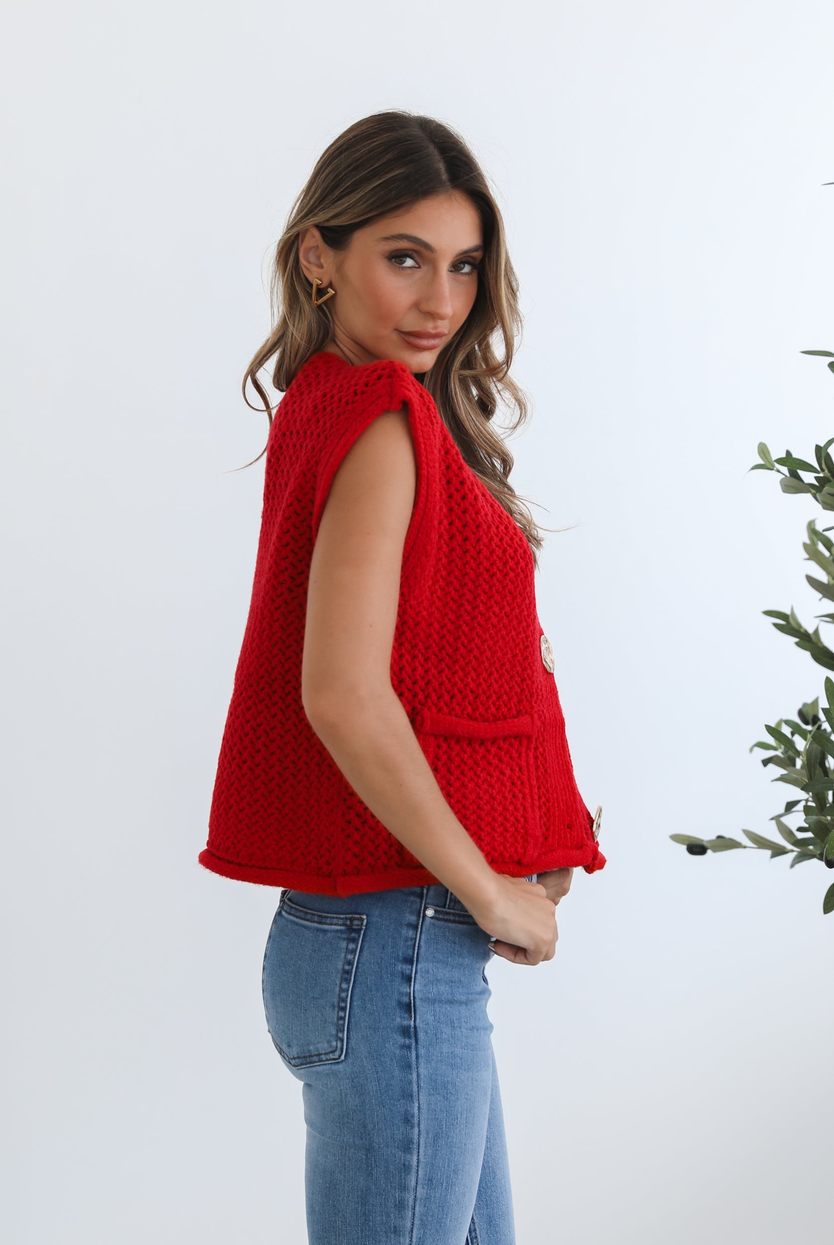 A woman wearing a red knit top with round neckline and center-front buttons, paired with blue jeans.