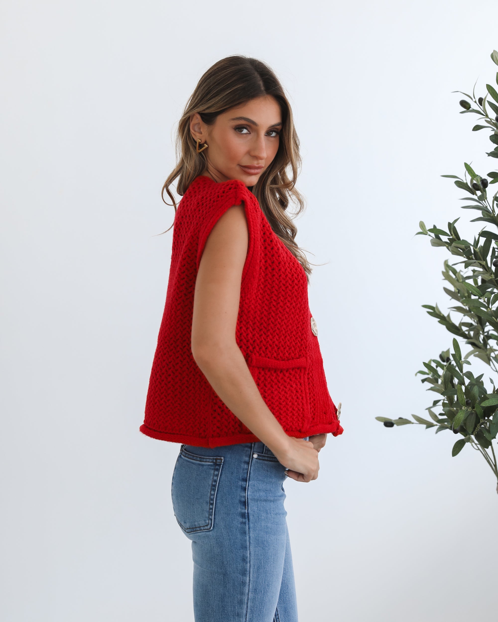 A woman wearing a red knit top with round neckline and center-front buttons, paired with blue jeans.